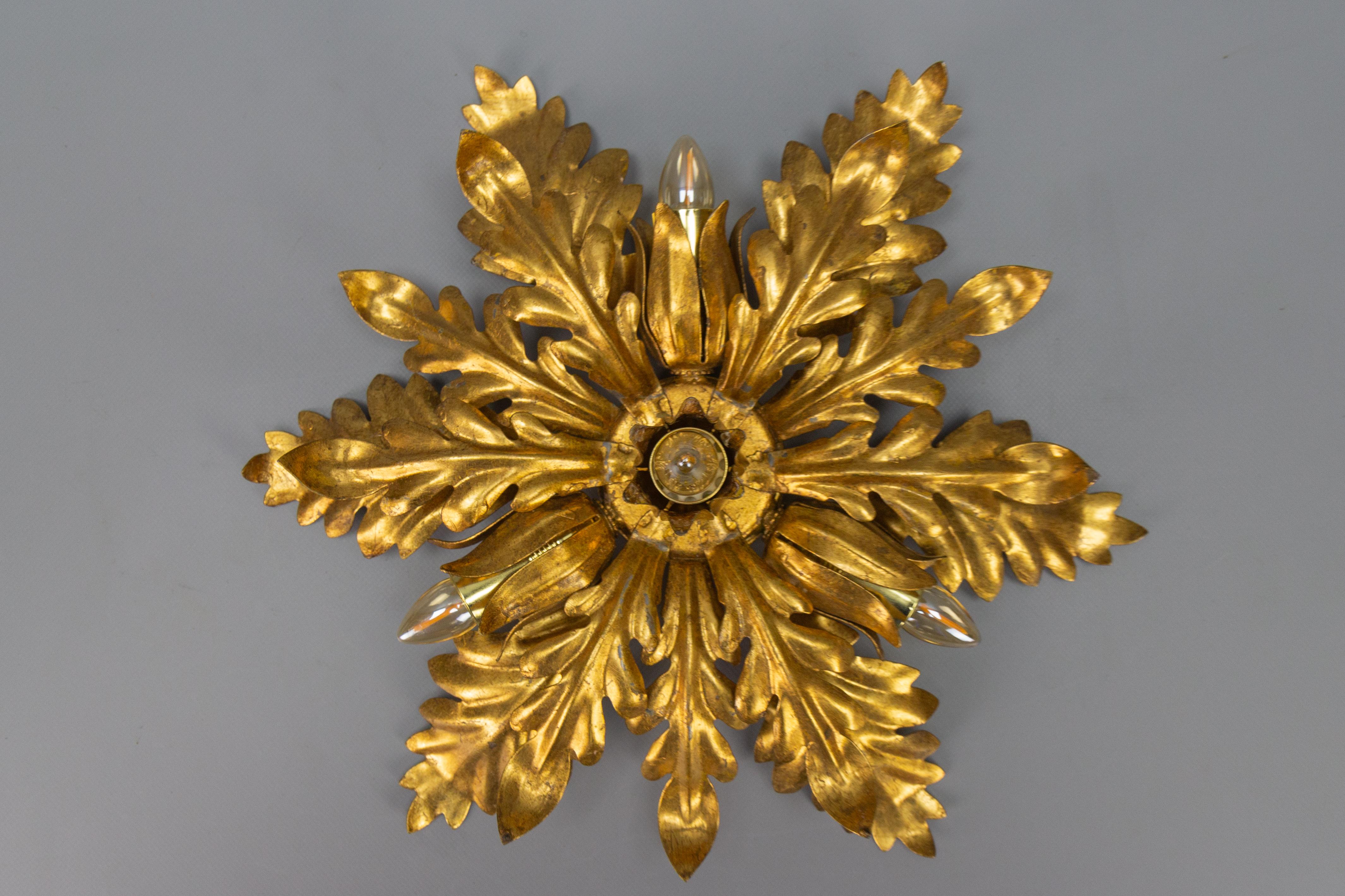 Gilt metal leafed sunburst-shaped four-light flush mount or wall lamp, circa the 1970s.
This adorable Hollywood Regency-style gilt metal flush mount is ornate with beautifully sculpted golden leaves that form a shape of a sunburst or large flower.
