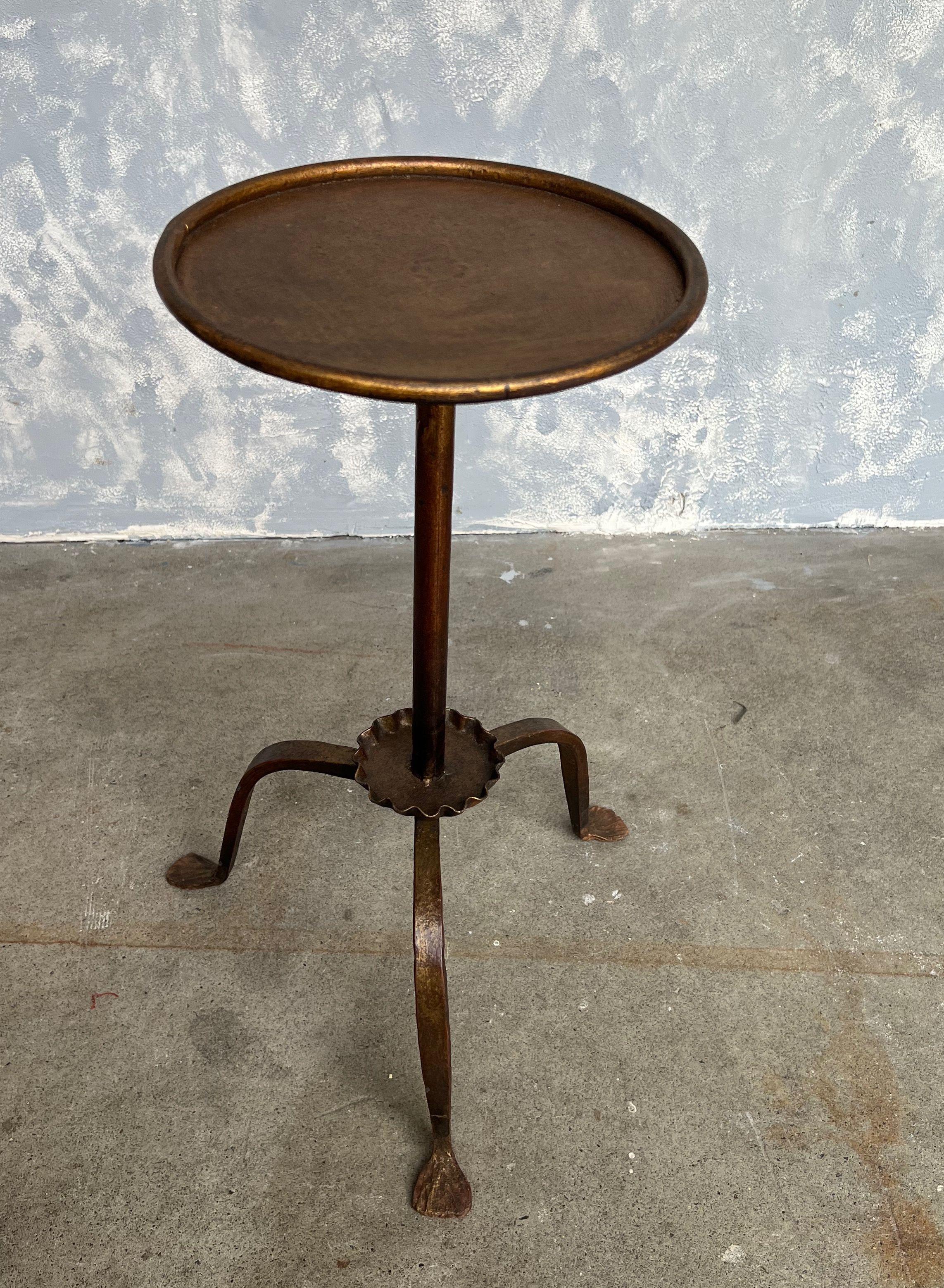 This gilt iron drinks table is replete with elegance, featuring a unique ruffled bobeche that artfully connects the round top, encased in a rolled frame, to the simple yet graceful tripod base. The original finish is a hand-applied gold patina with