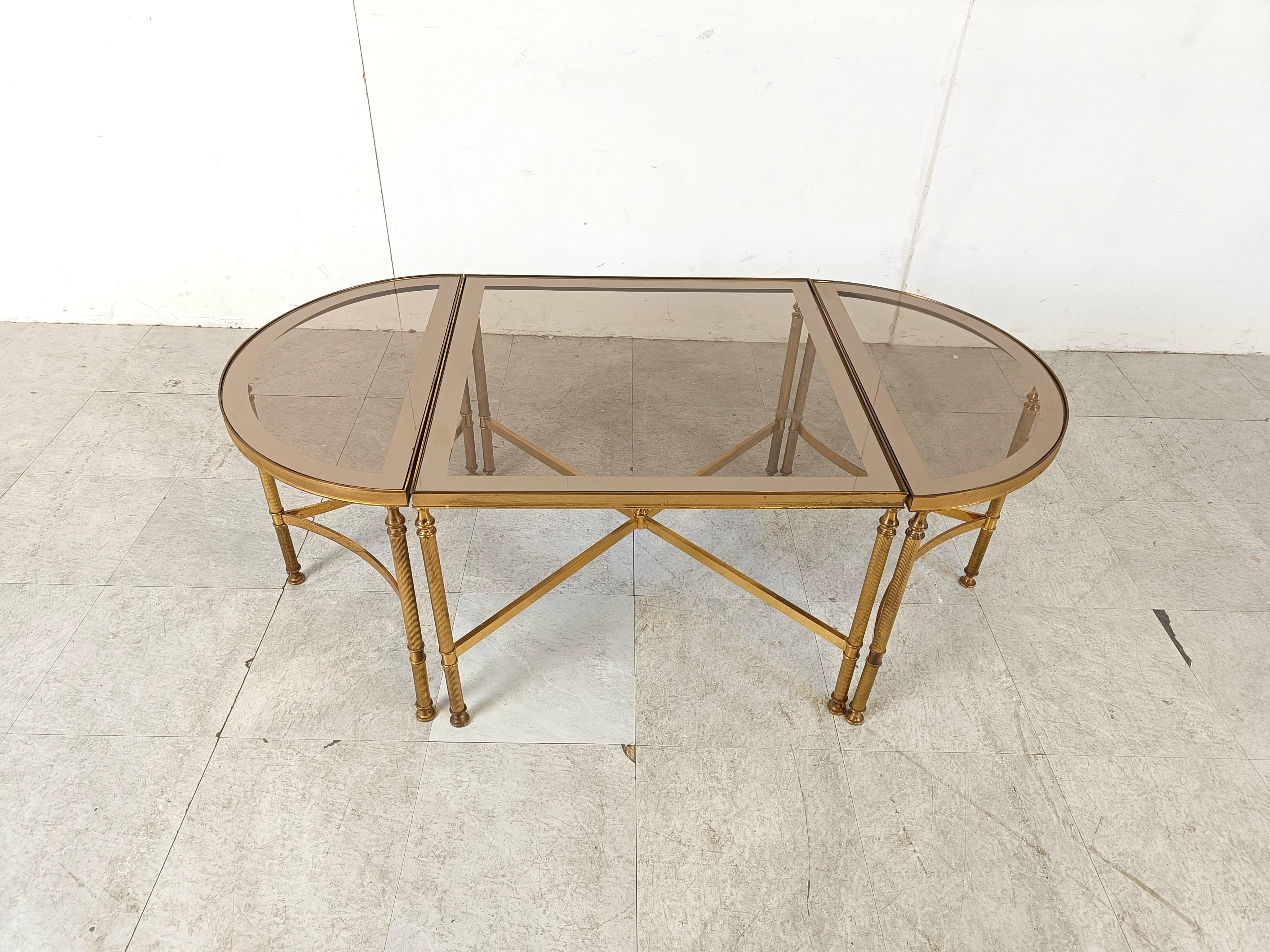 Neoclassical coffee table set consisting of three tables with a gilt metal frame and smoked glass top with mirrored edges in the manner of Maison Jansen.

Playful design with the bent metal between the legs.

The two side tables can be used