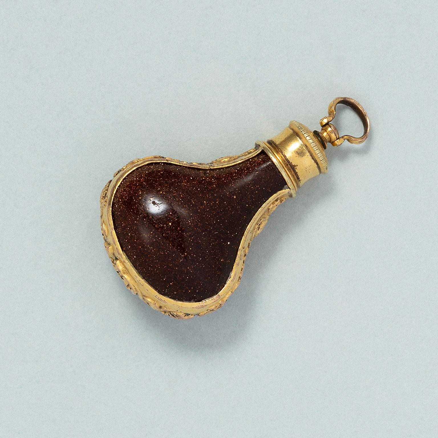 A jug-shaped perfume bottle made of goldstone with a gilded screw cap and a border decorated with shells, foliage and floral ornament along the sides of the bottle, 18th century.

weight: 7.18 g
dimensions: 2.9 x 1.8 x 1.1 mm