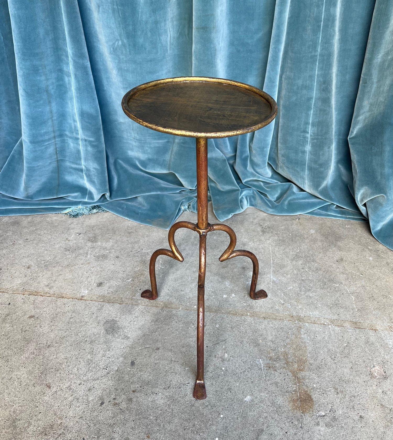 An elegant gilt iron drinks table with gracefully curved legs on a tripod base. The tripod base with its unusual design and hand-applied gold patina with red undertones adds a touch of elegance to any room. This unique side table dates back to the