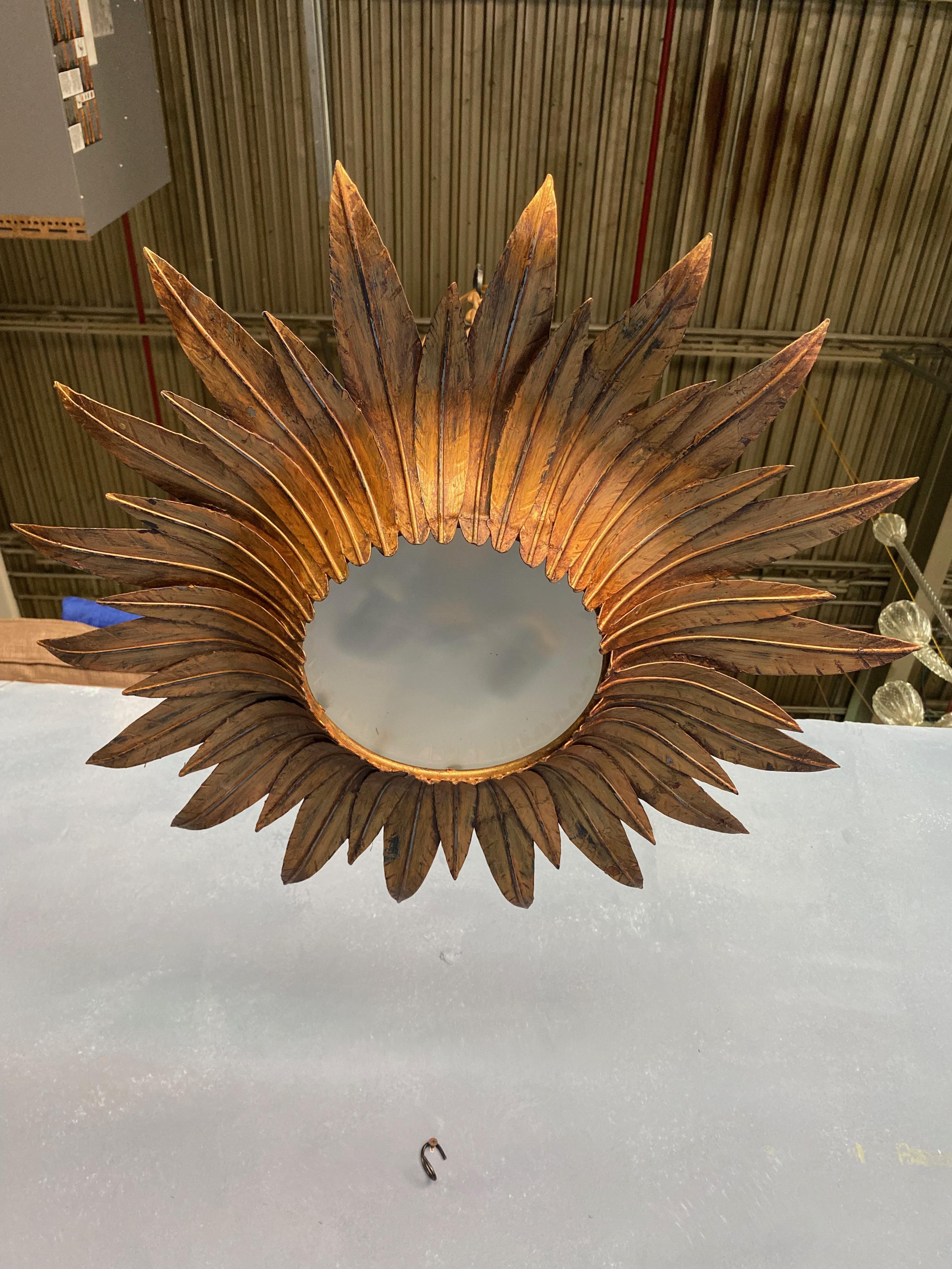 This impressive flush mount ceiling fixture, originating from Spain in the 1950s, features an intricate design of alternating longer and shorter feathered rays. These rays are closely grouped together, framing a round acid-etched glass diffuser. The