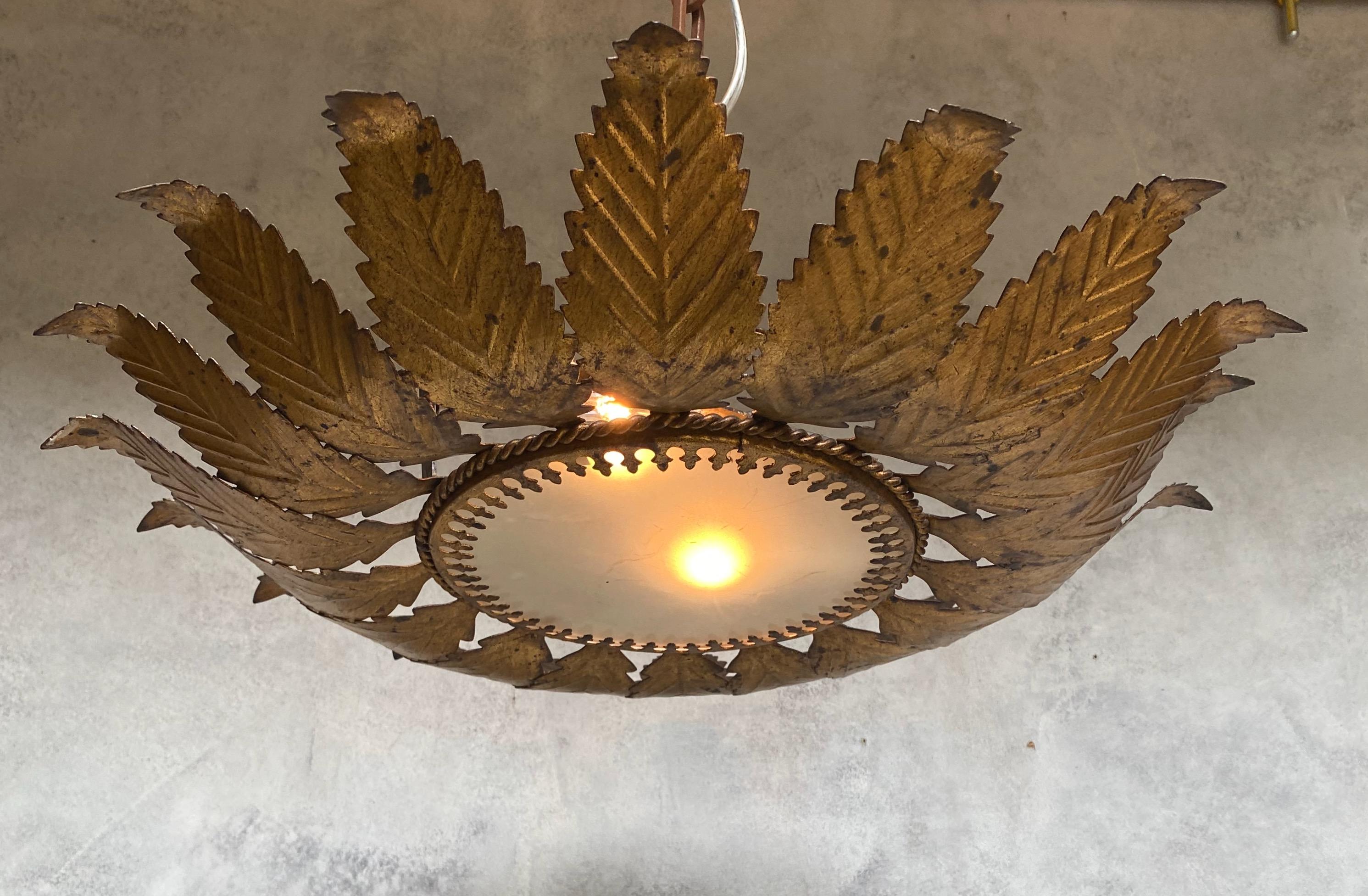 A stunning gilt metal sunburst ceiling fixture from Spain dating back to the 1950s. This flush mount ceiling fixture is composed of eighteen leaf patterned radiating rays joined at the base with a single braid and a decorative interior band that