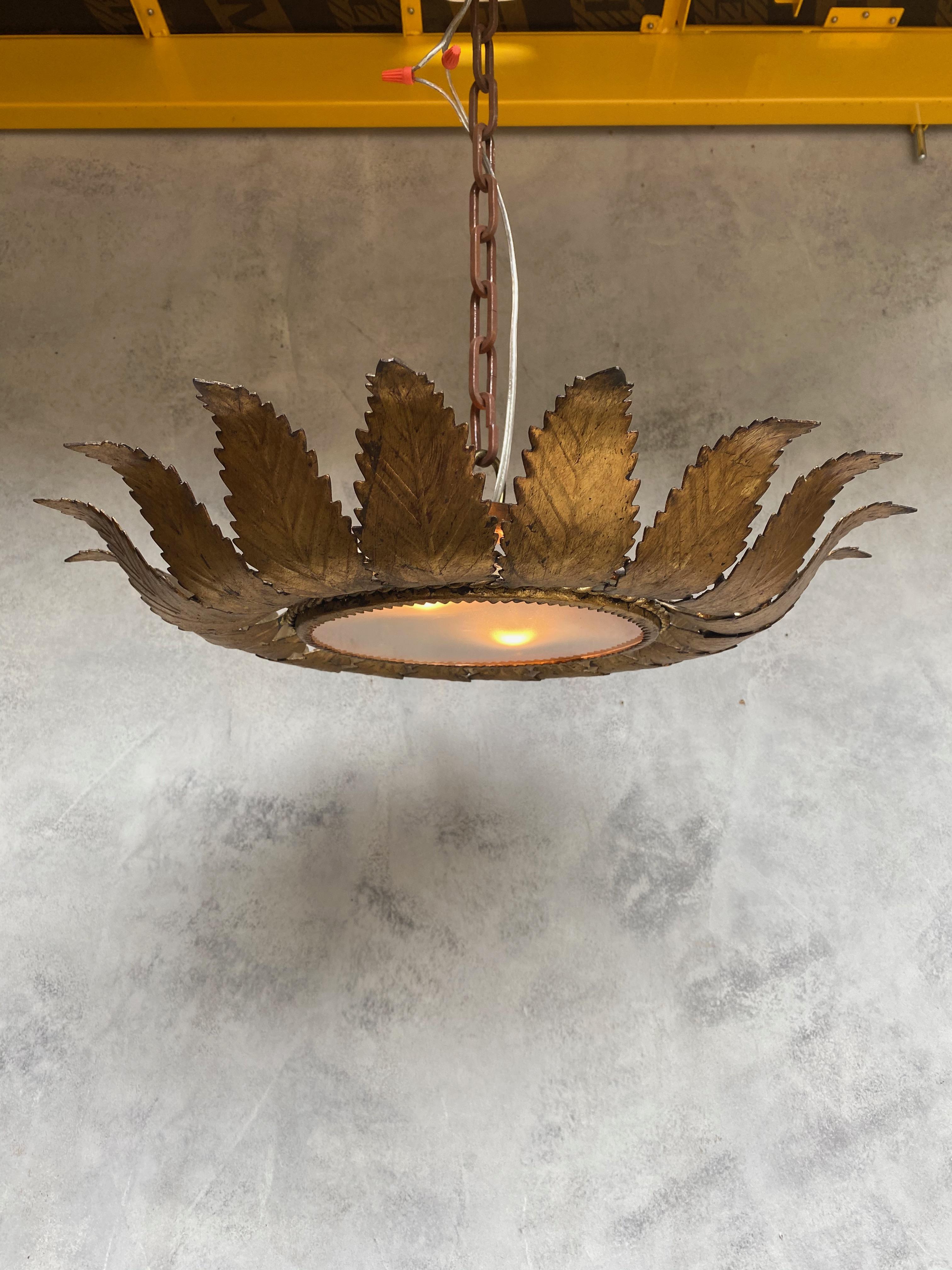 This stunning gilt metal sunburst ceiling fixture from 1950s Spain features eighteen stylized feathered rays that radiate from its core. Each ray is masterfully joined at the base by a single braid, further accentuated by an eye-catching tetrafoil