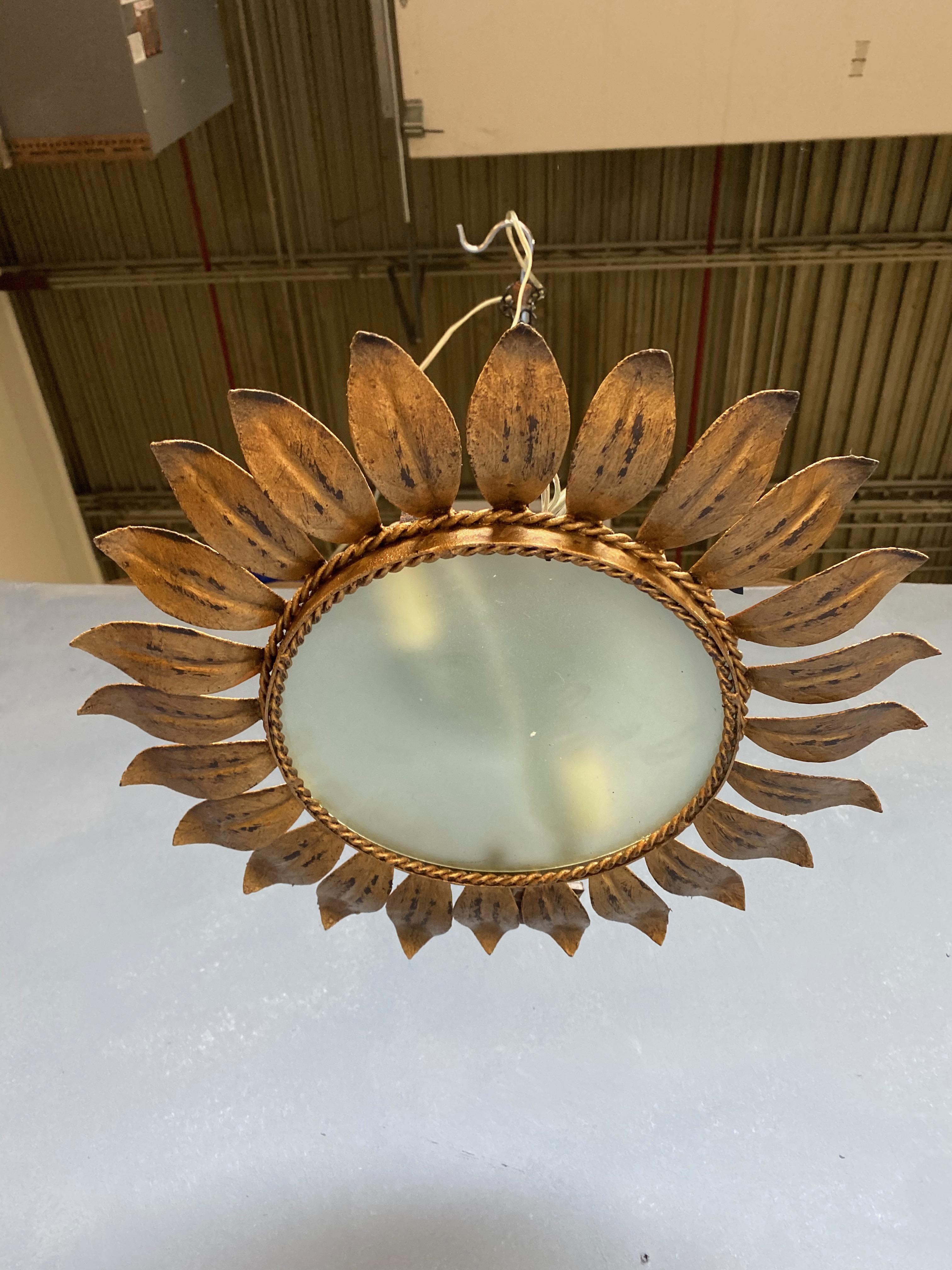 A small flush mount ceiling fixture with closely joined leaf motifs radiating from a raised center circle and framed by 4 strands of twisted braiding. The hand applied finish has a rich gold patina over a darker under coat. This fixture has been