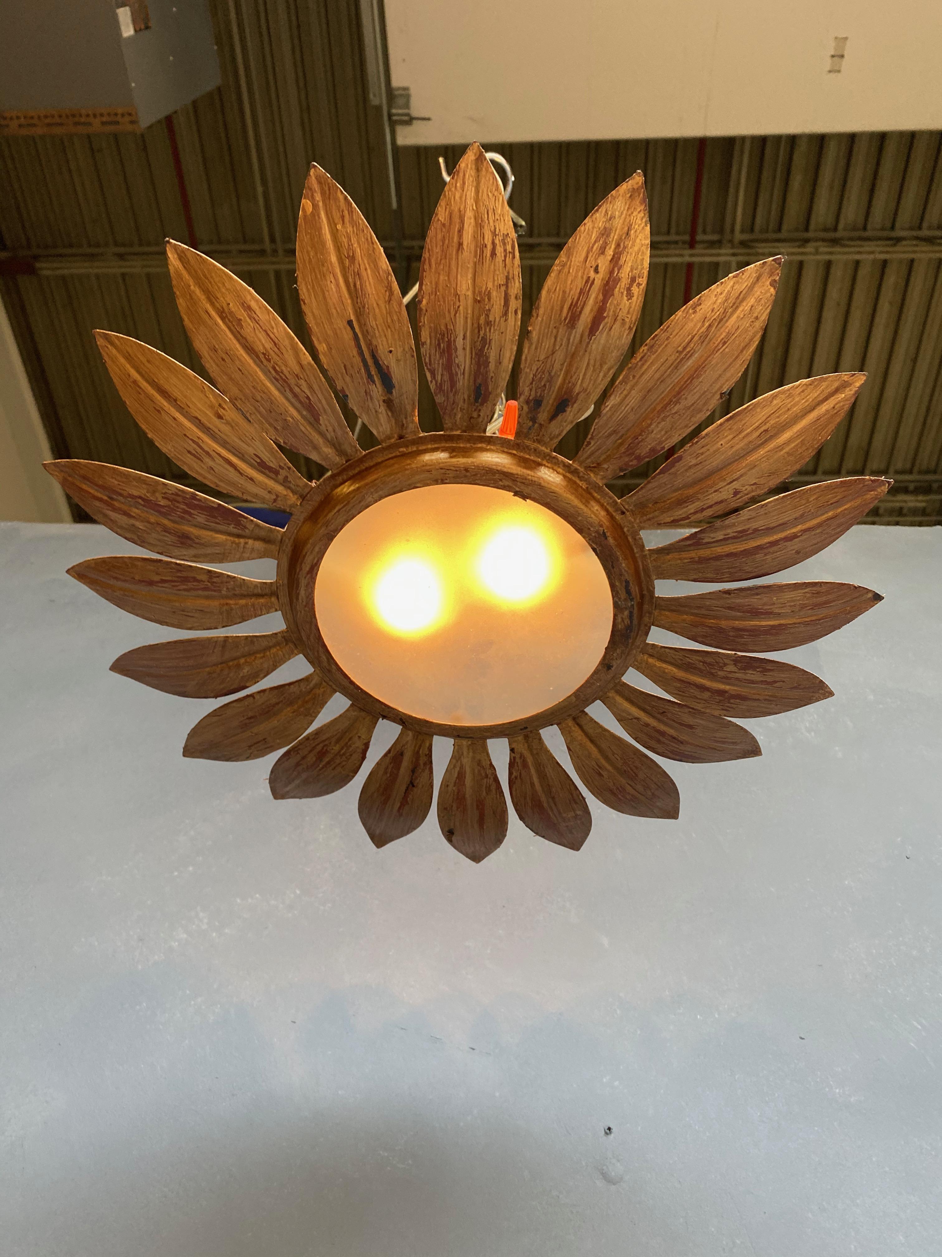 A small flushmount ceiling fixture with closely joined leaf motifs radiating from a solid center circle. The hand applied finish has a rich gold patina over a darker red under coat. This fixture has been recently wired to accommodate 2 candelabra