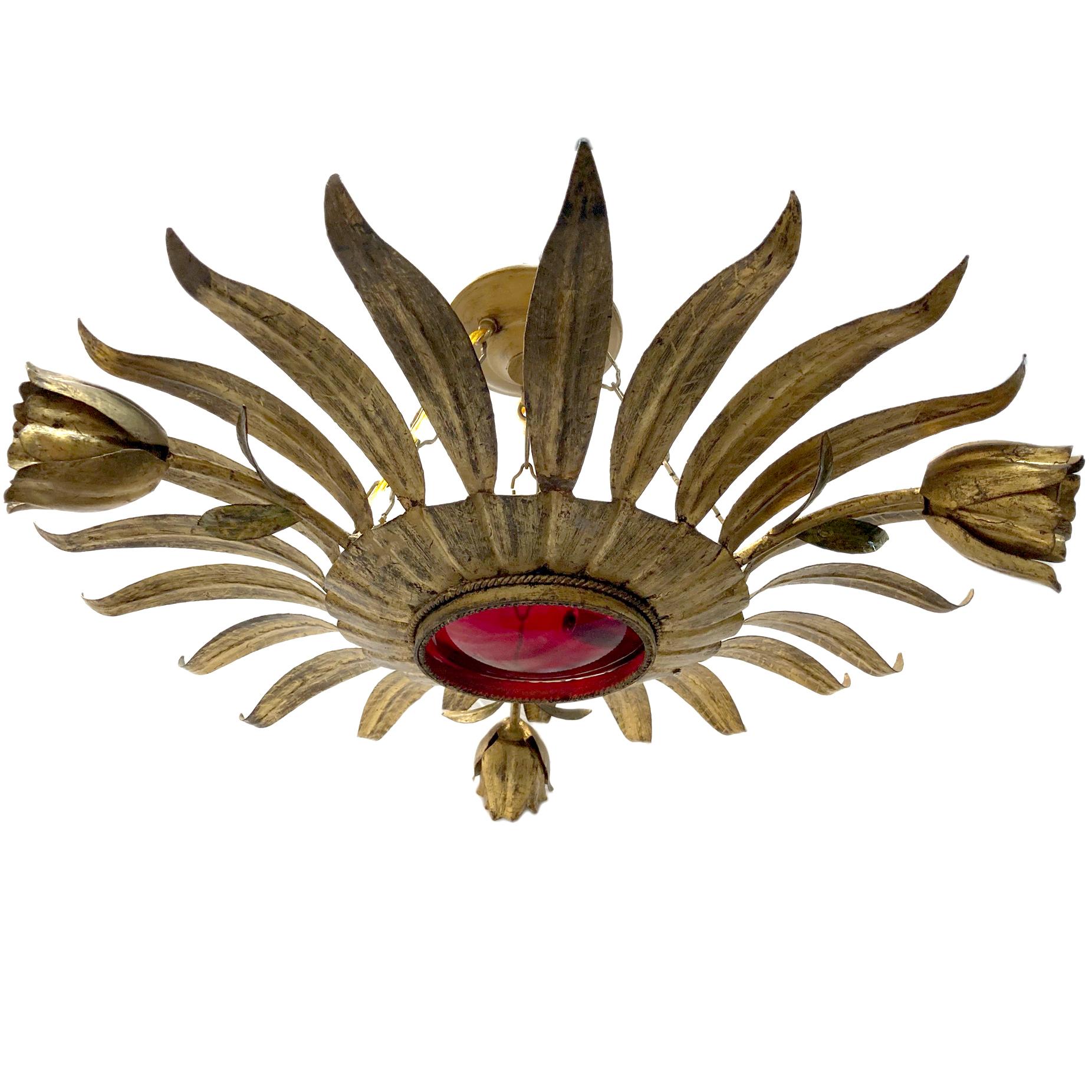 A circa 1950's gilt metal sunburst light fixture with four interior candelabra lights, one light in each flower and original ruby red glass inset.

Measurements:
Diameter: 24