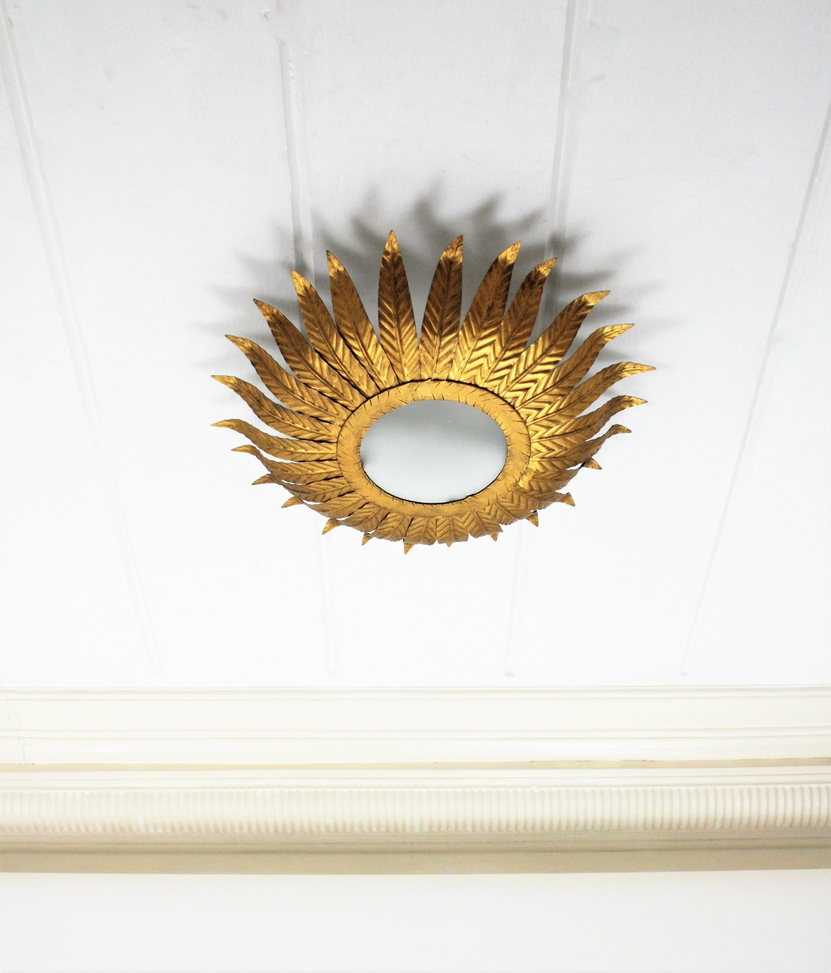 Gilt metal sunburst leafed flushmount or sunburst mirror, Spain, 1960s.
This beautiful ceiling light fixture features a flower burst / sunburst comprised by leaves surrounding a central frosted glass difusser. It can be used as flushmount or as a