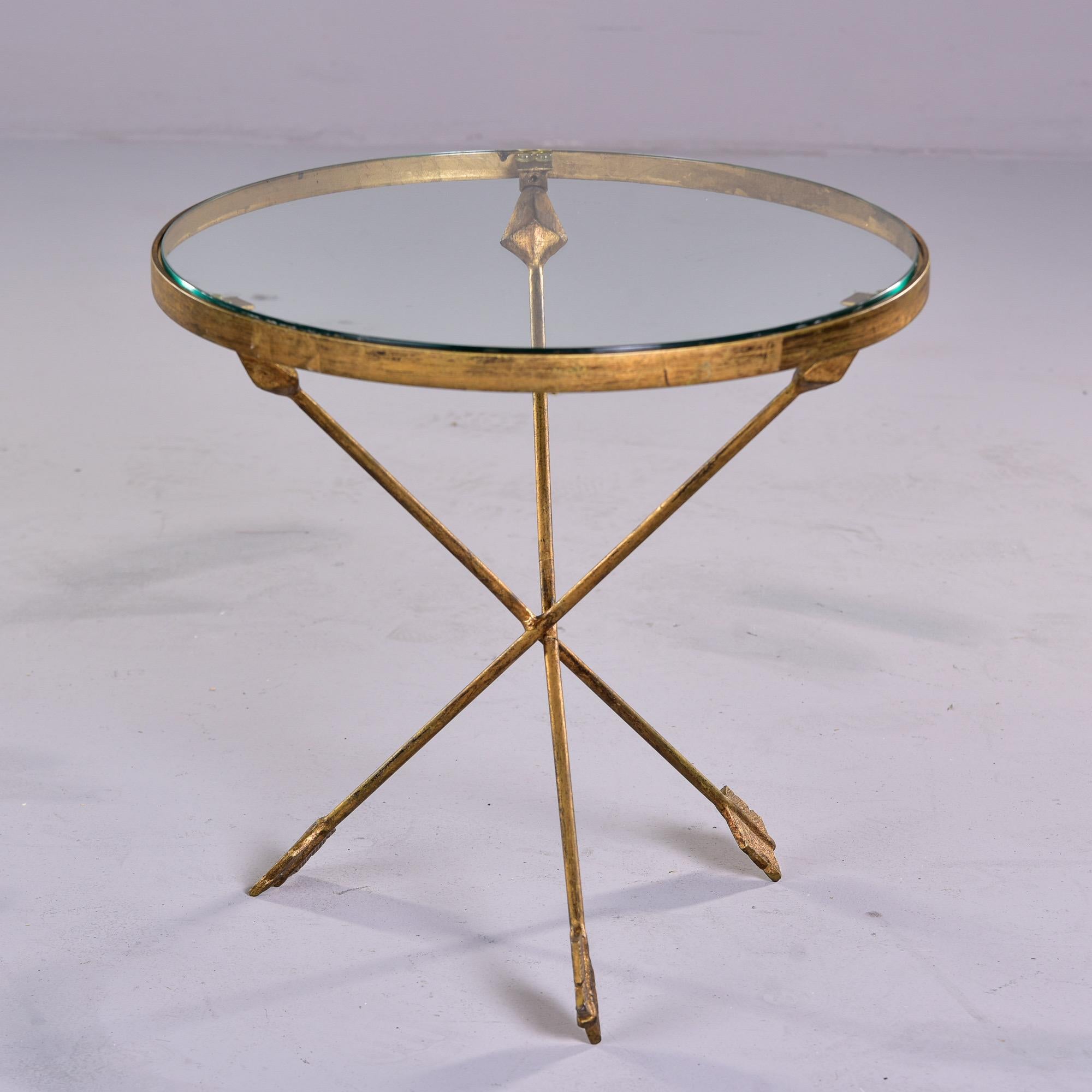 French circa 1960s side or accent table with a round glass top and gilded iron base in the form of three crossed arrows. Unknown maker. Very good vintage condition. 

 