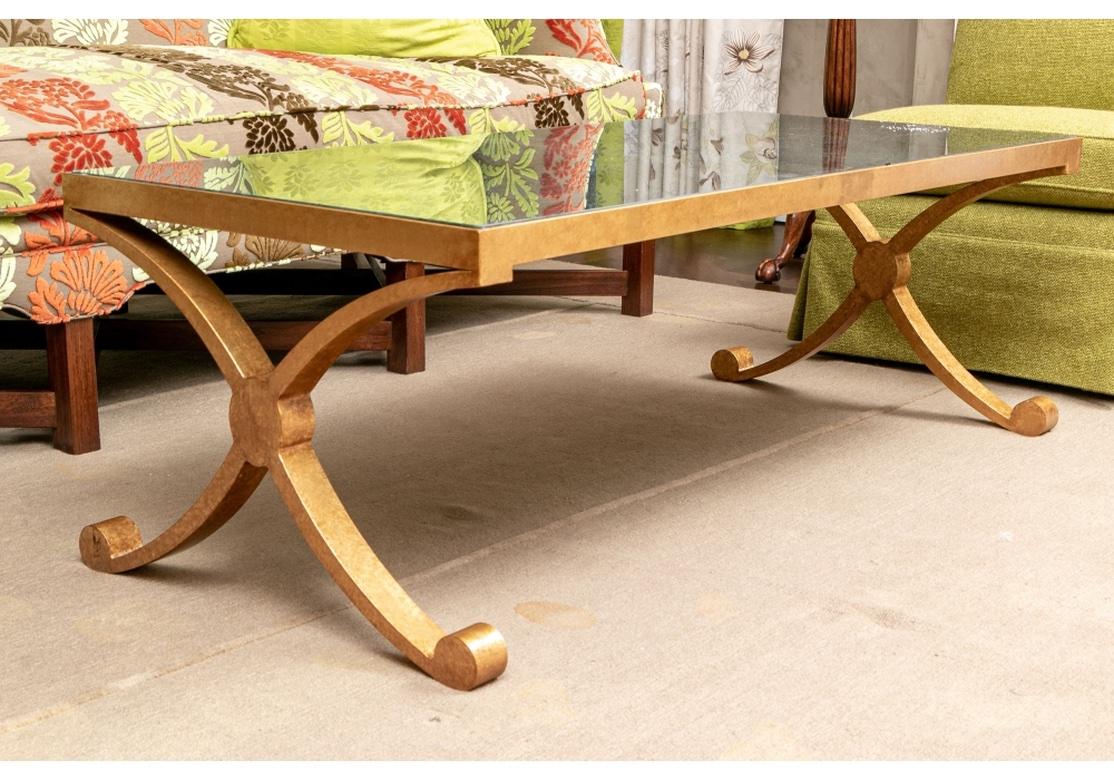 With fine Stylized Classical form.  X Form Cocktail Table by David Iatesta in the manner of  the Hollywood Regency style. The metal frame in his antique mottled gold finish with curved X shaped side supports on scrolled feet. With an inset mottled