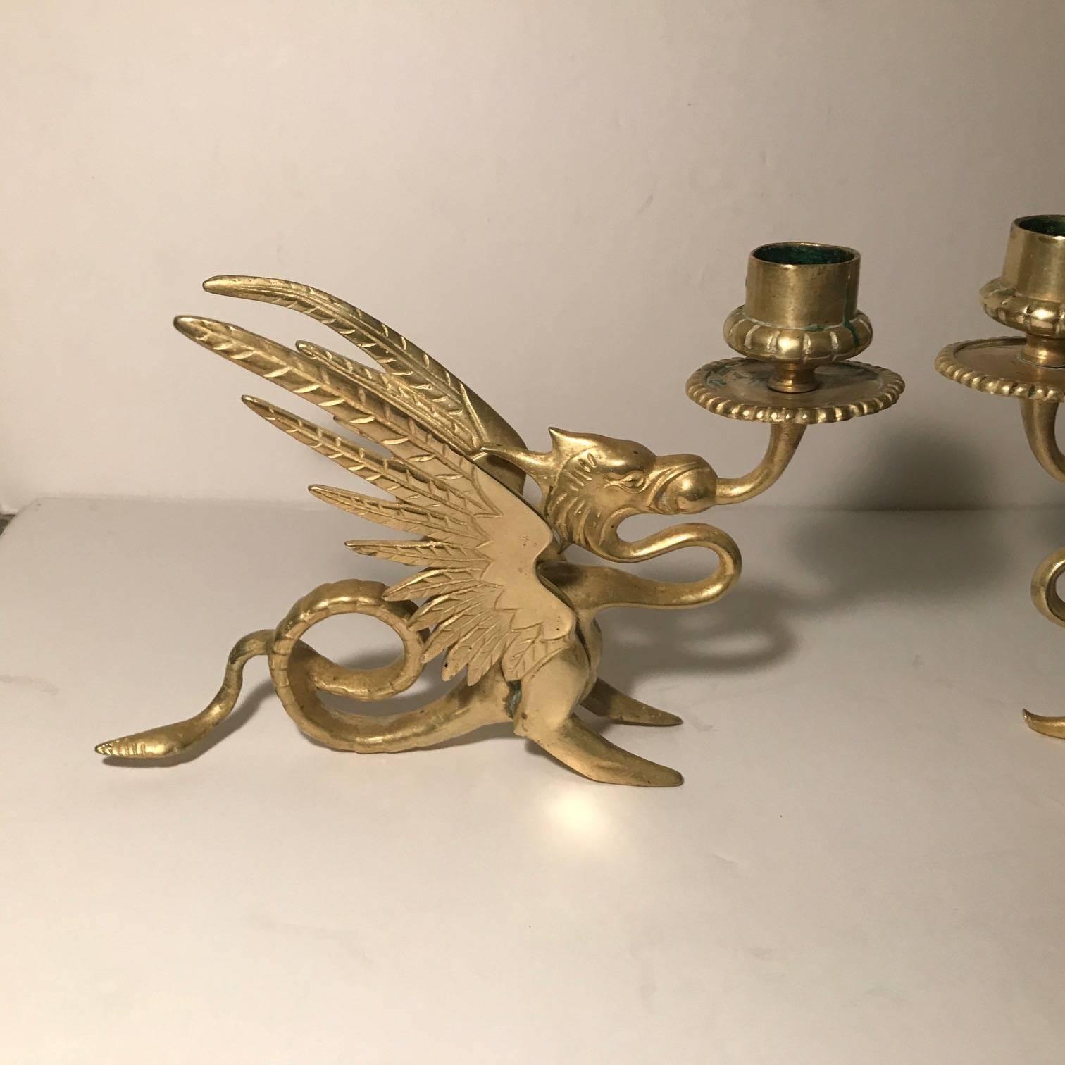 A pair of gilt brass Griffin motif candlesticks. The winged figure with a curled tail which is the finger ring to use as a chamber stick.