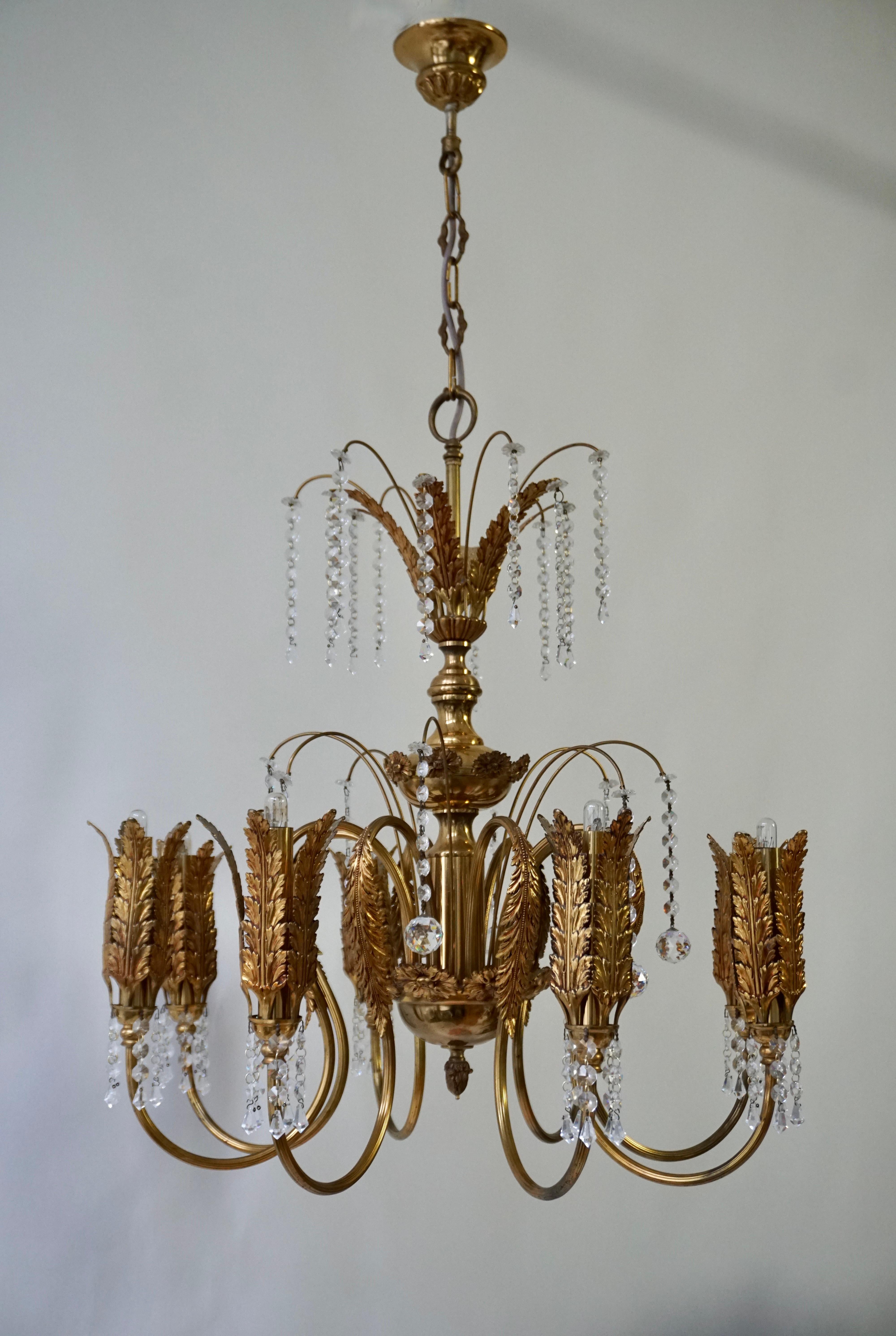  A opulent, gilt metal, Hollywood Regency chandelier. The finish has a rich, gleaming tone, and the unique shape changes from various points of view. Palm leaves sprout from the column and bottom ball and the end of each arm.
The chandelier is