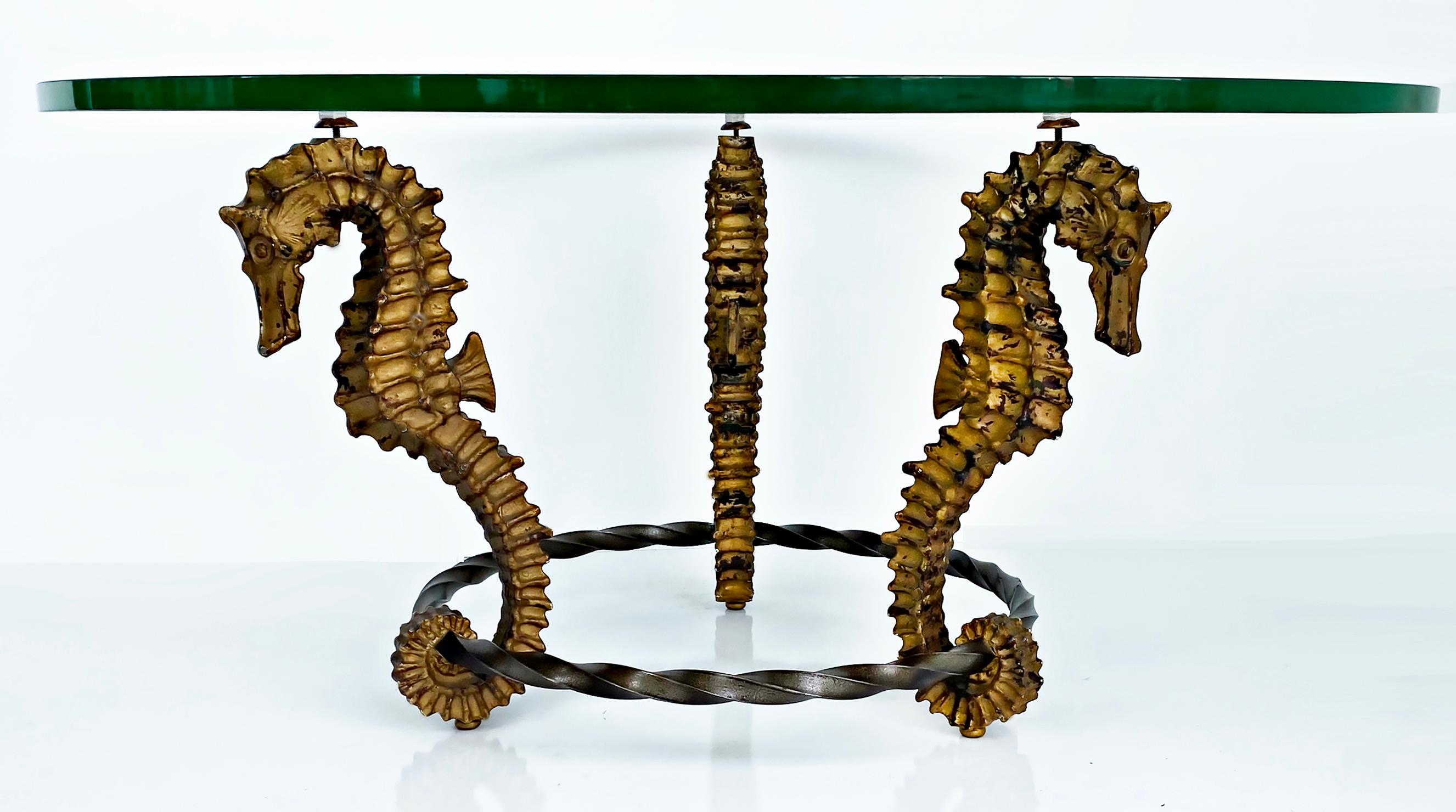 Gilt seahorse coffee table with thick round glass top, iron and metal

Offered for sale is a circa 1970s modern coffee table supported by three gilt metal seahorses connected by a twisted iron ring at the base. The seahorses support a thick round