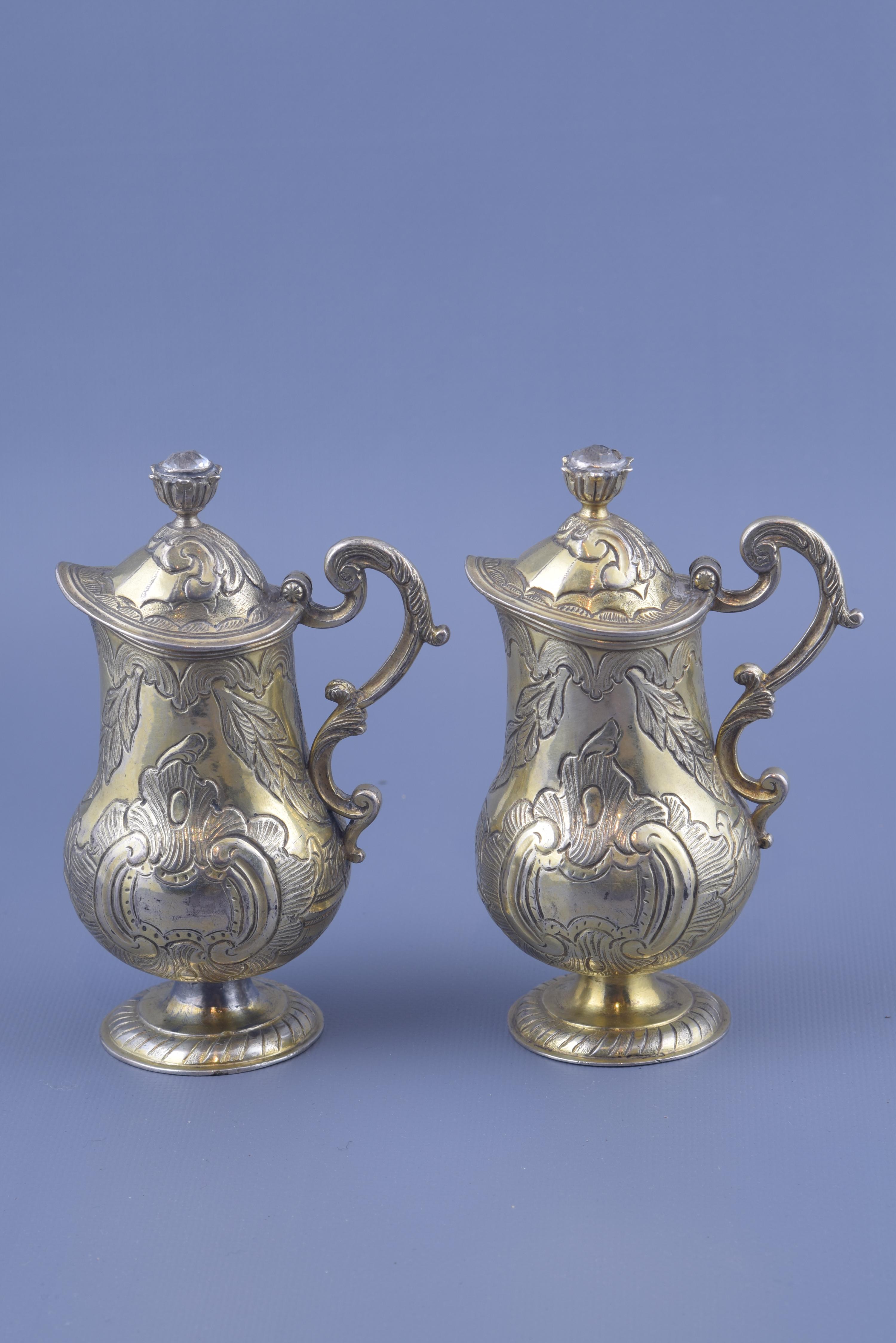Pair of jars with lid and handle made in silver gilt. A circular base (decorated with moldings and lines parallel to each other) gives way to a smooth foot, from which arises the body of the piece (circular in its lower area and tubular in the