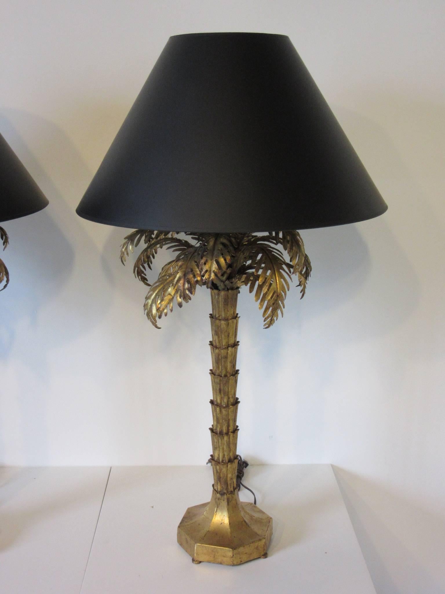 A pair of gold gilt metal Tole palm tree table lamps with detailed leaves and trunks , black satin shades with gold toned molt interiors . Designed in the manner of Maison Jansen and Hollywood Regency. Measurement of the bottom of the shades base is