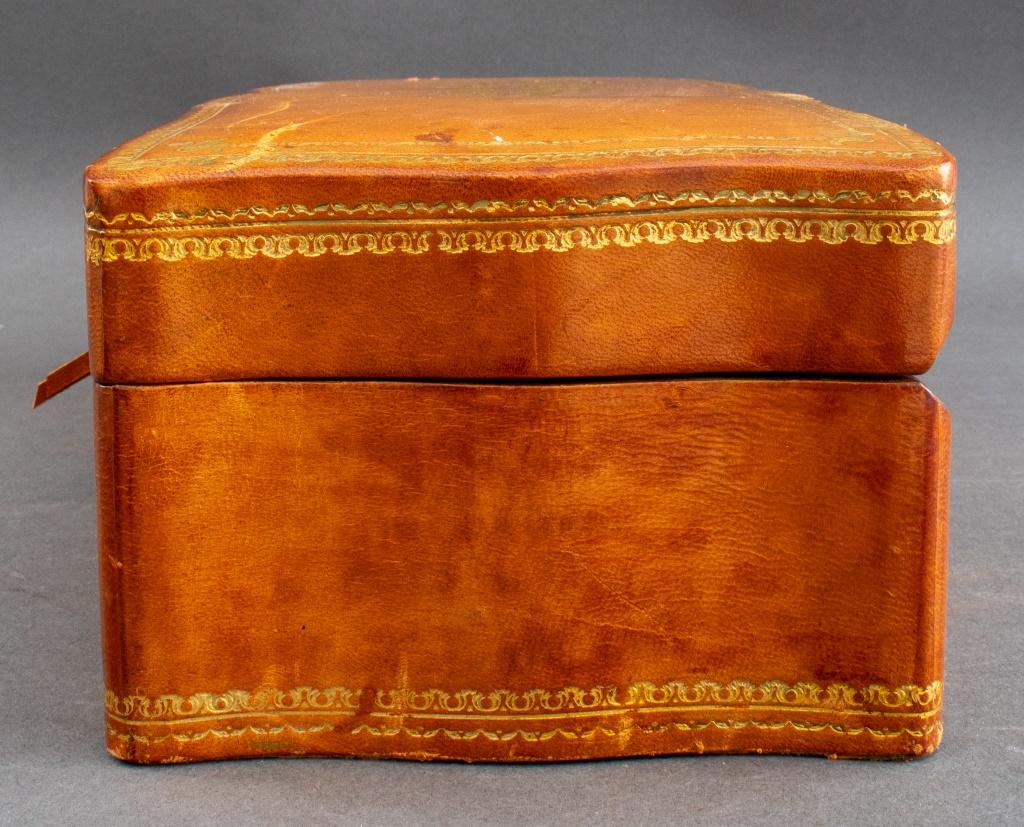 Gilt tooled leather covered jewelry box, the shaped elongated rectangular box with gilt-tooled edges and center, opening to reveal an olive velvet fitted interior.  4.25