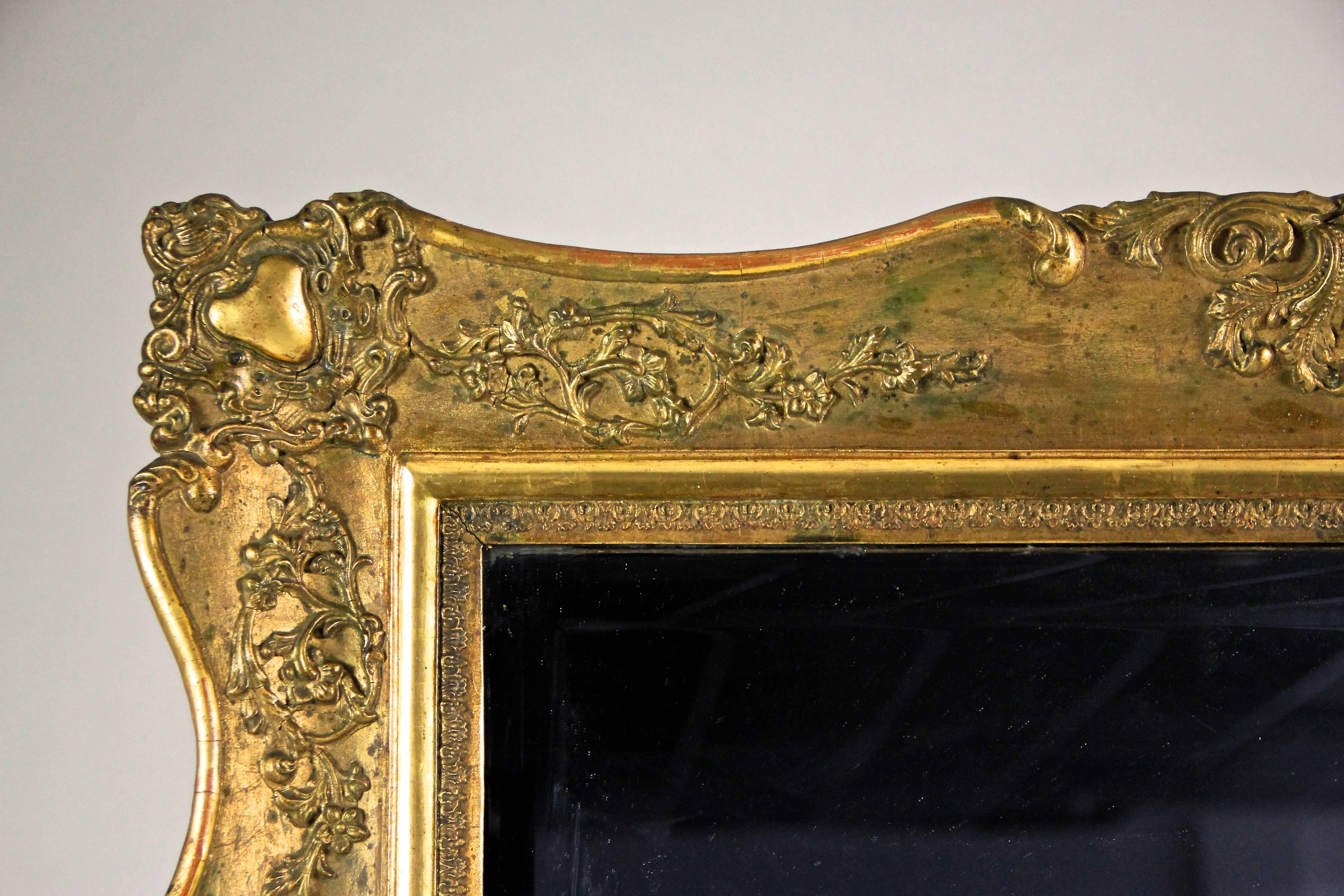 Large gilt wall mirror from the Biedermeier period in Austria from the early 19th century, circa 1830. The gilt artful processed frame is adorned by beautiful floral stucco works and covered by an absolute great looking patina. The mirror glass,