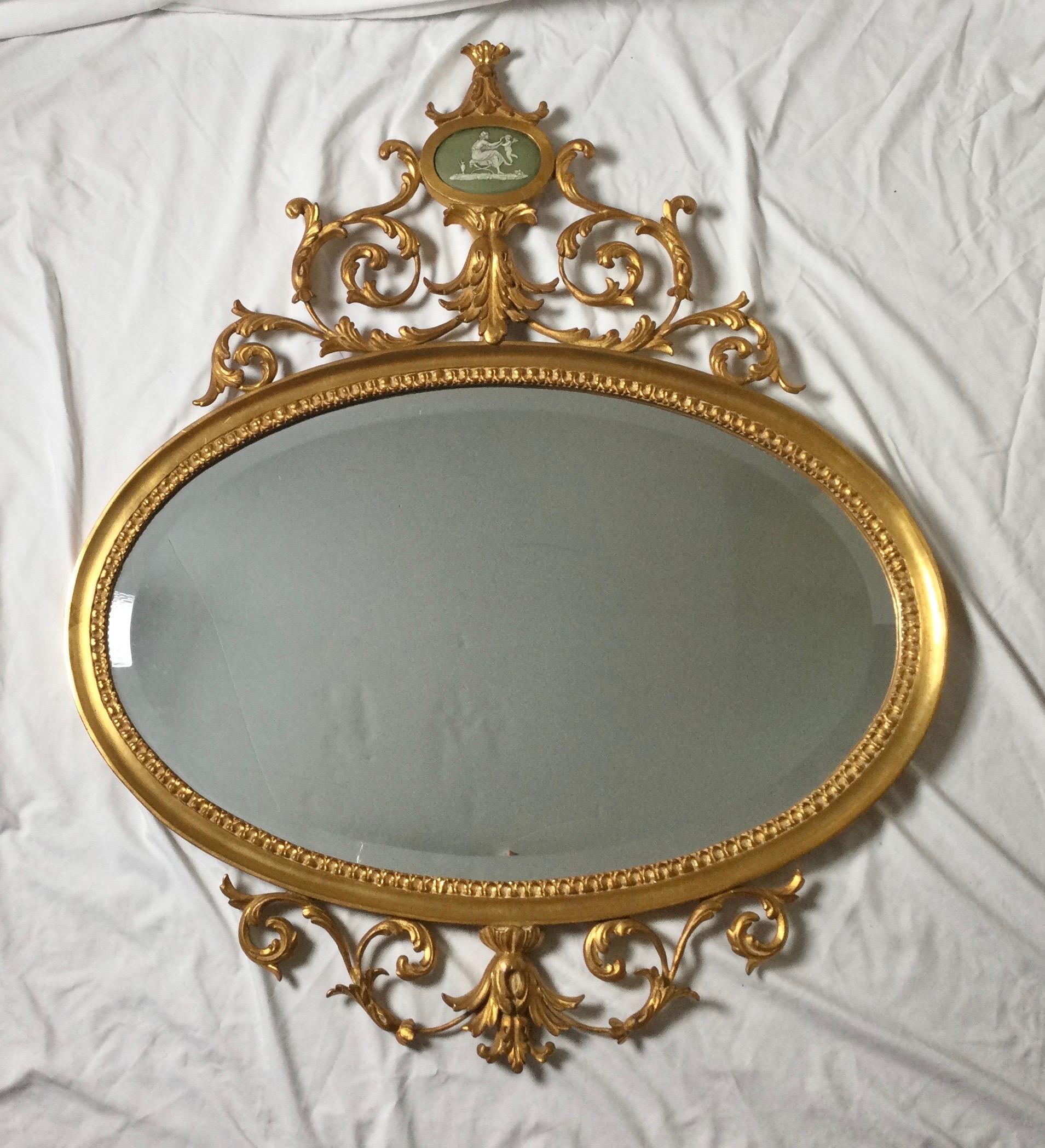 Elegant Louis XV style oval mirror in gilt wood.. The elaborate from with a center cartouche at the pediment painted to look like Jasperware. The mirror with an elegant bevel.