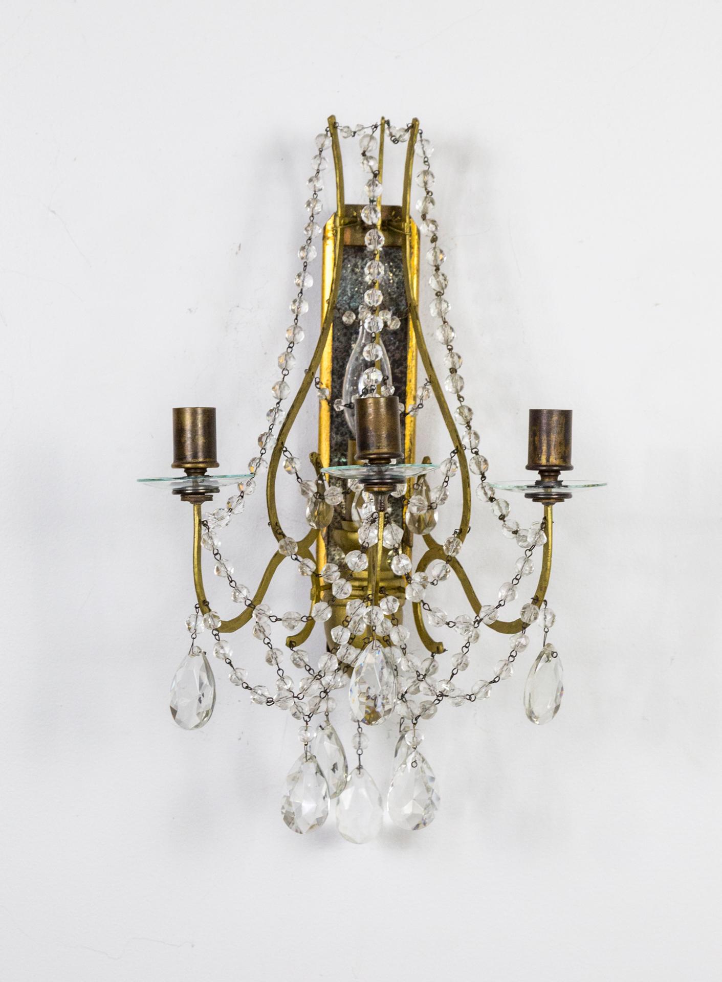 A Belle Epoque pair of highly decorative sconces with original antique mirror on gilded wood back plates with urn details, glass bobeches, and crystal beading. One middle candelabra light (60w max) and 3 candle holders (candles not included).