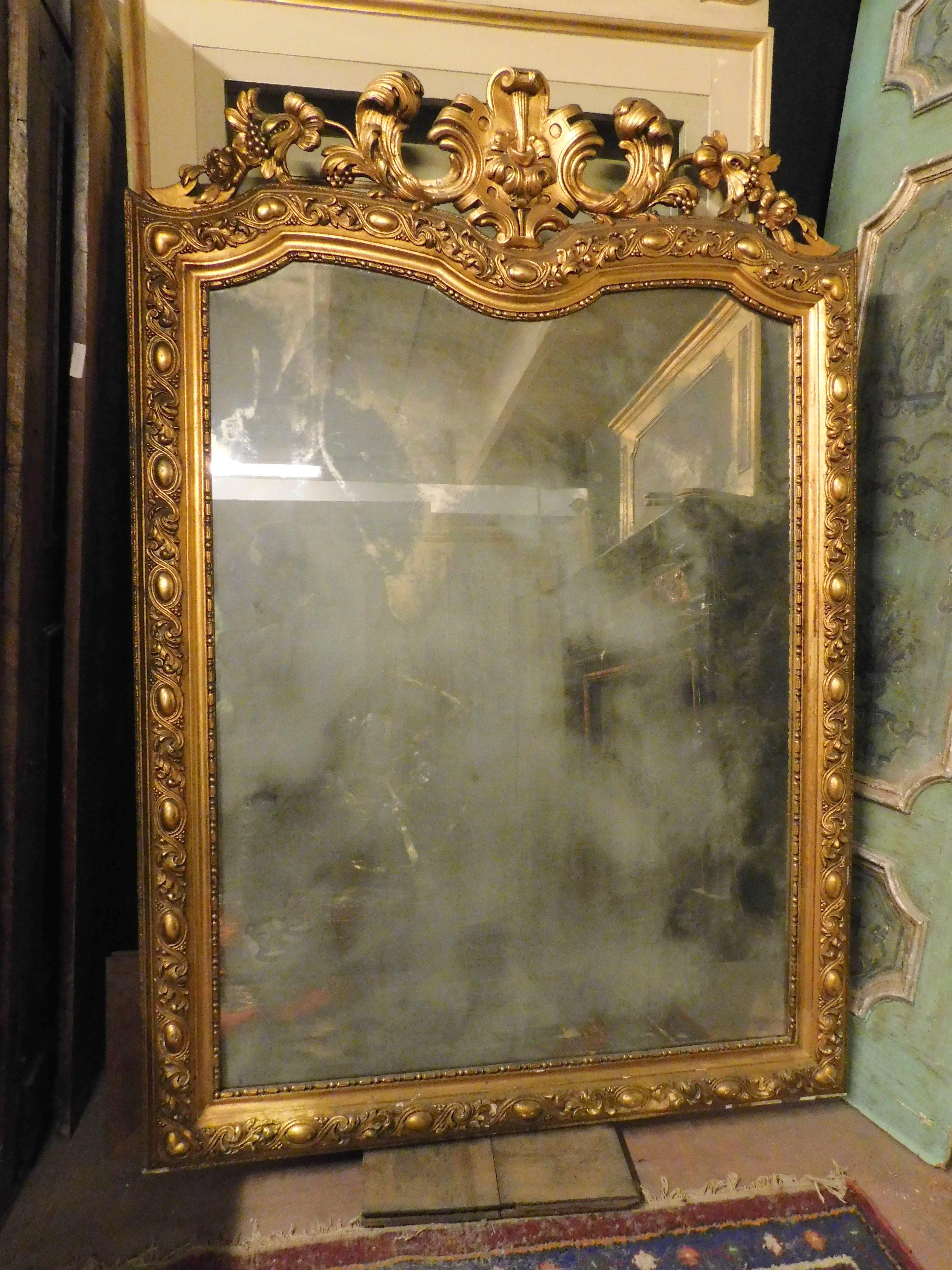 Ancient wooden mirror, richly gilded and with sculpted cymatium, with original opaque mirror, built in the 19th century in Italy, originally placed above a fireplace, it can be adapted both to the wall and above a historic piece of furniture or