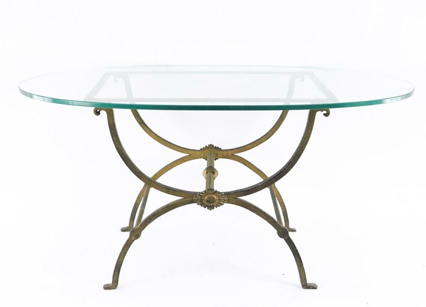 The elegant coffee table is a modern interpretation of neoclassical design. The base is composed of curved gilt wrought iron while the oval top is made of clear glass. Perfect for the porch or patio.