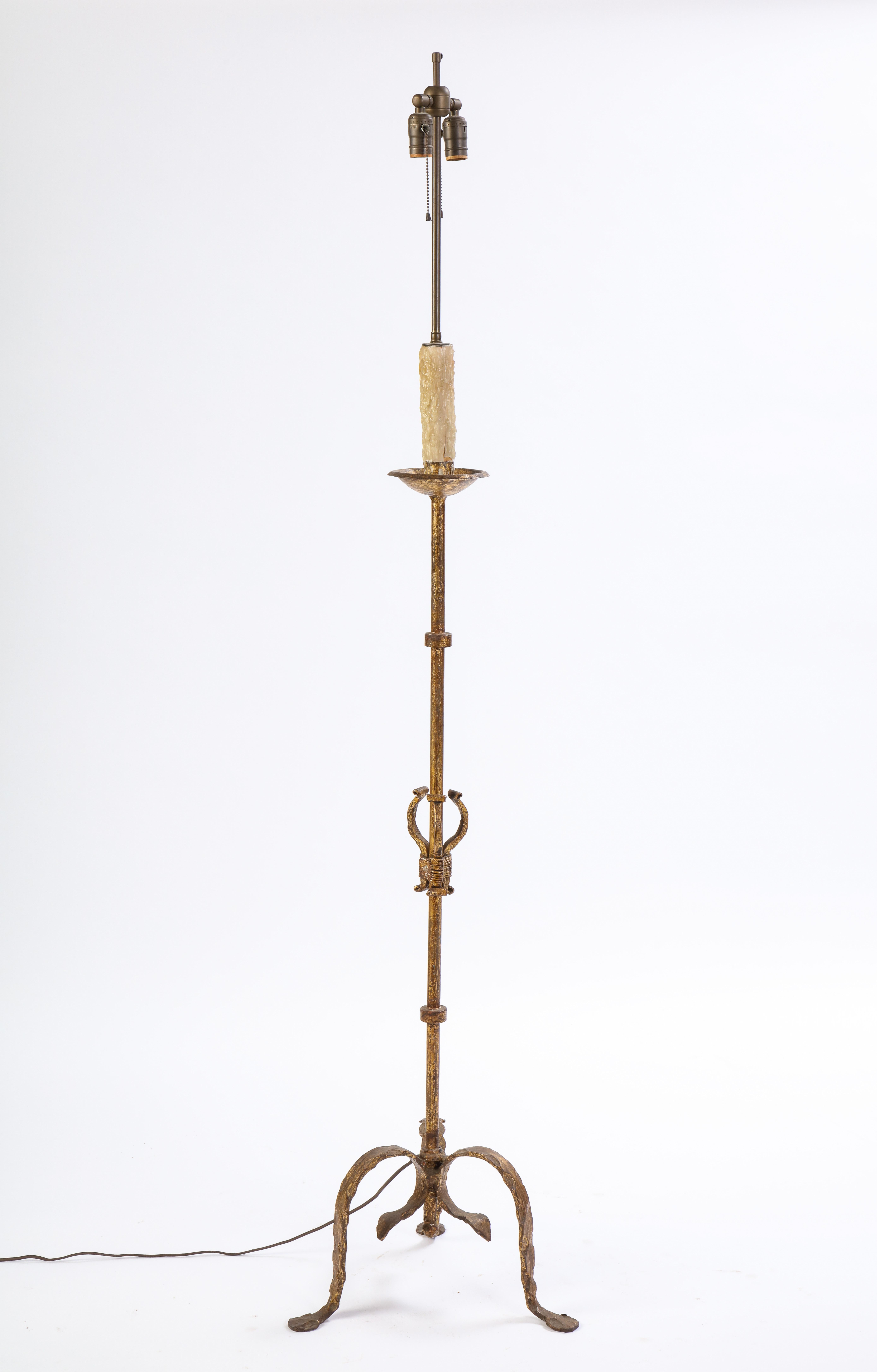 This gilt wrought-iron, modern large floor lamp, is raised on three molded legs with padded feet. It features a twisted wrought-iron stand and feet, with decorative scroll work detail and a faux beeswax candle in the center. 71.5 inches in height.