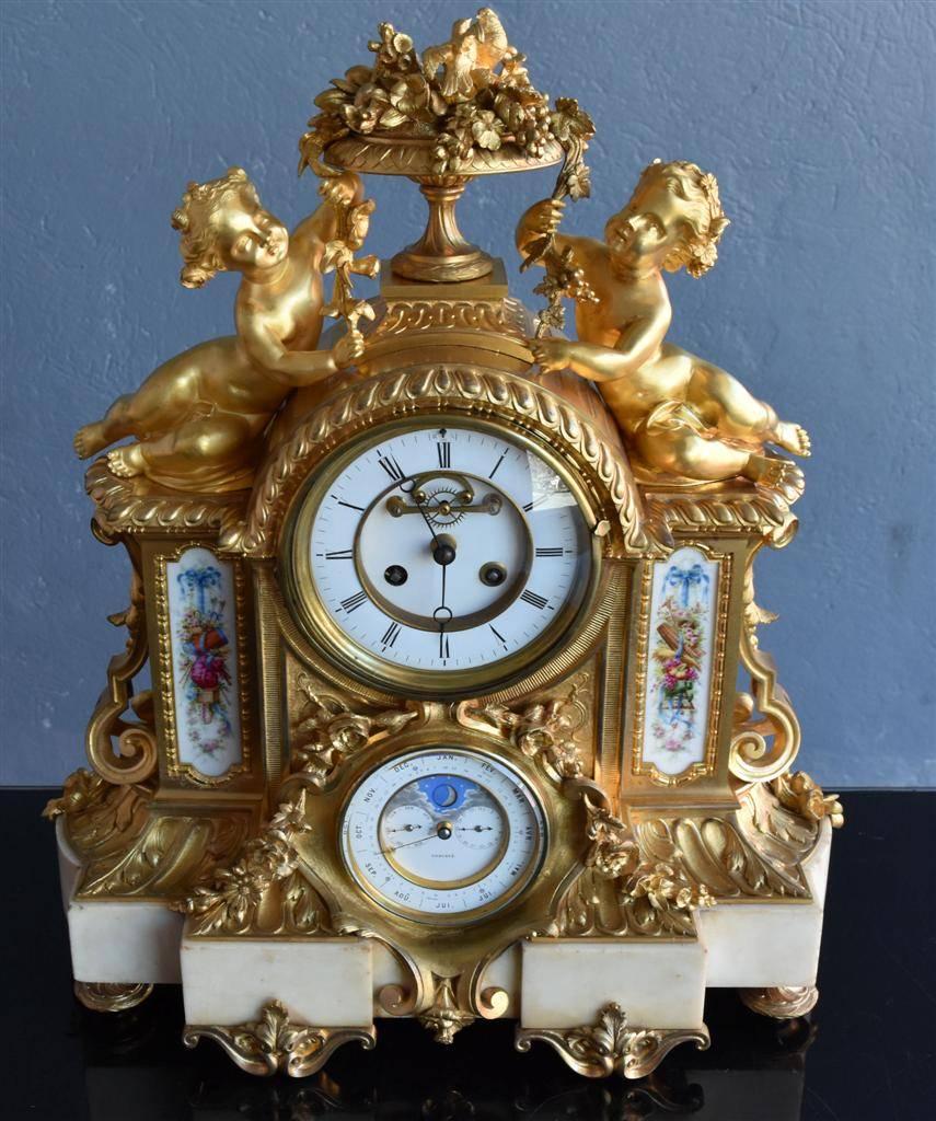 XIXth century gilded clock for mantel embellishment, from the Napoleon III time, in the style of Louis XVI, with calendar and moon phase dial. 
Remarkable mercury gilding decorated witha  flower painted porcelain plate, and babies. the Candelabra