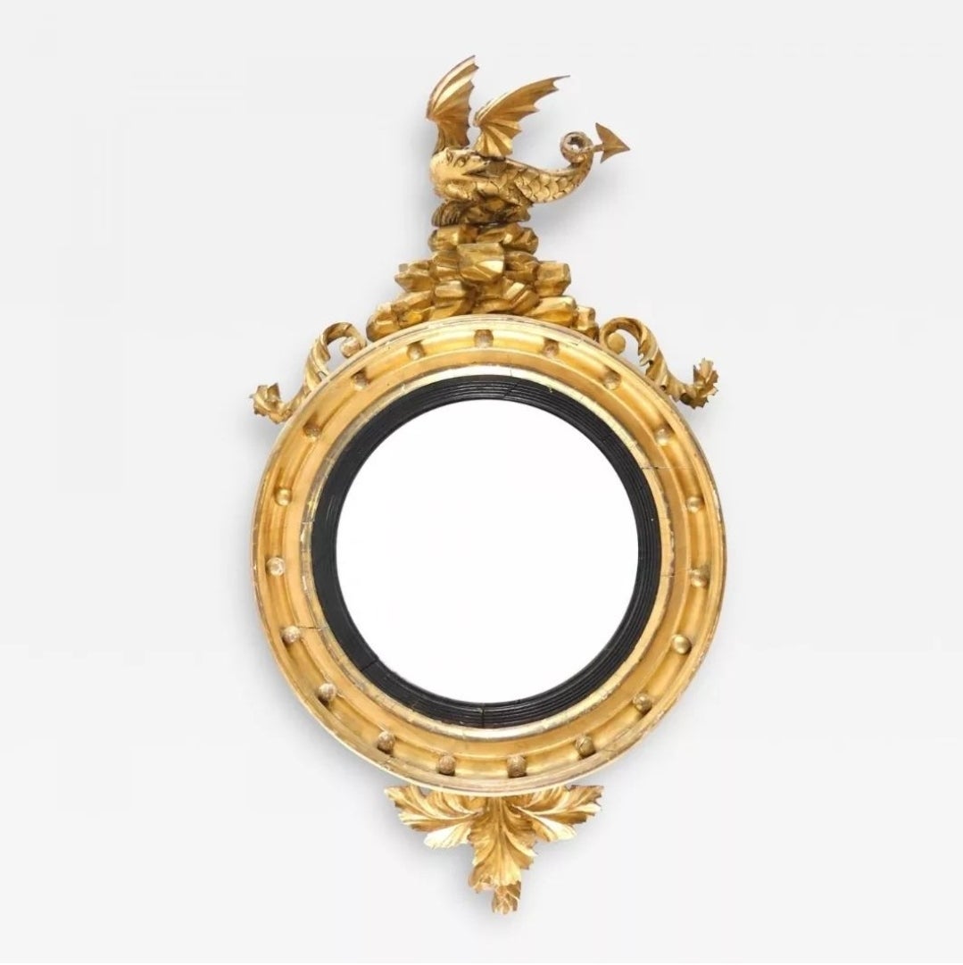 Regency carved giltwood convex mirror, circa 1820 in date.
The convex mirror is surrounded by an ebonized elegant reeded slip and a giltwood moulded frieze with ball mounts. The carved top pendant features a carved dragon perched atop a structure