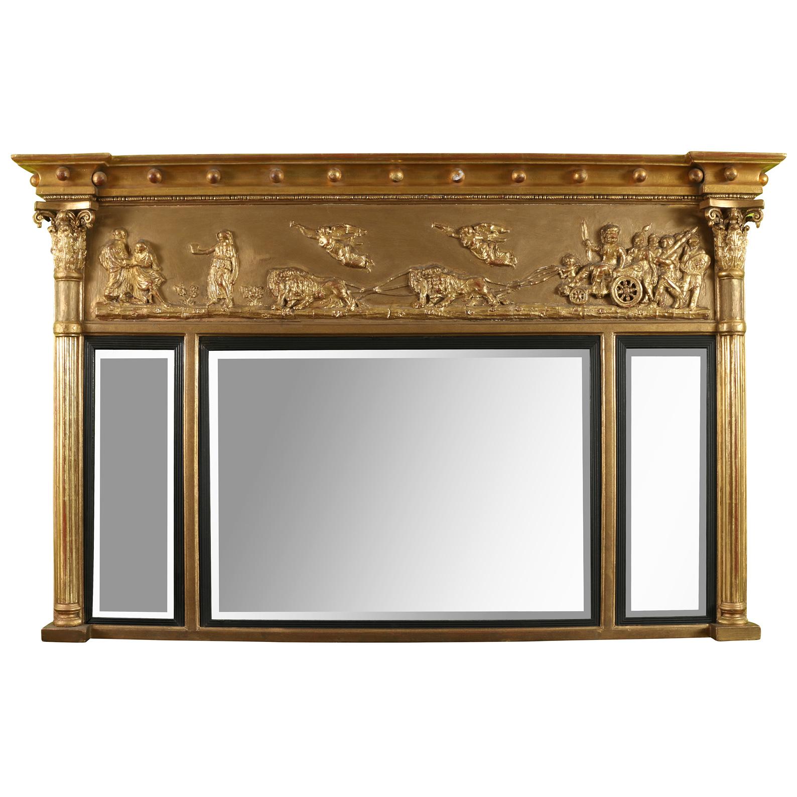 An elegant 19th-century Regency period giltwood  over mantel mirror consisting of three mirror sections flanked by reeded columns with intricately carved capitals.  The top section of the mirror is decorated with a mythological scene in exquisite