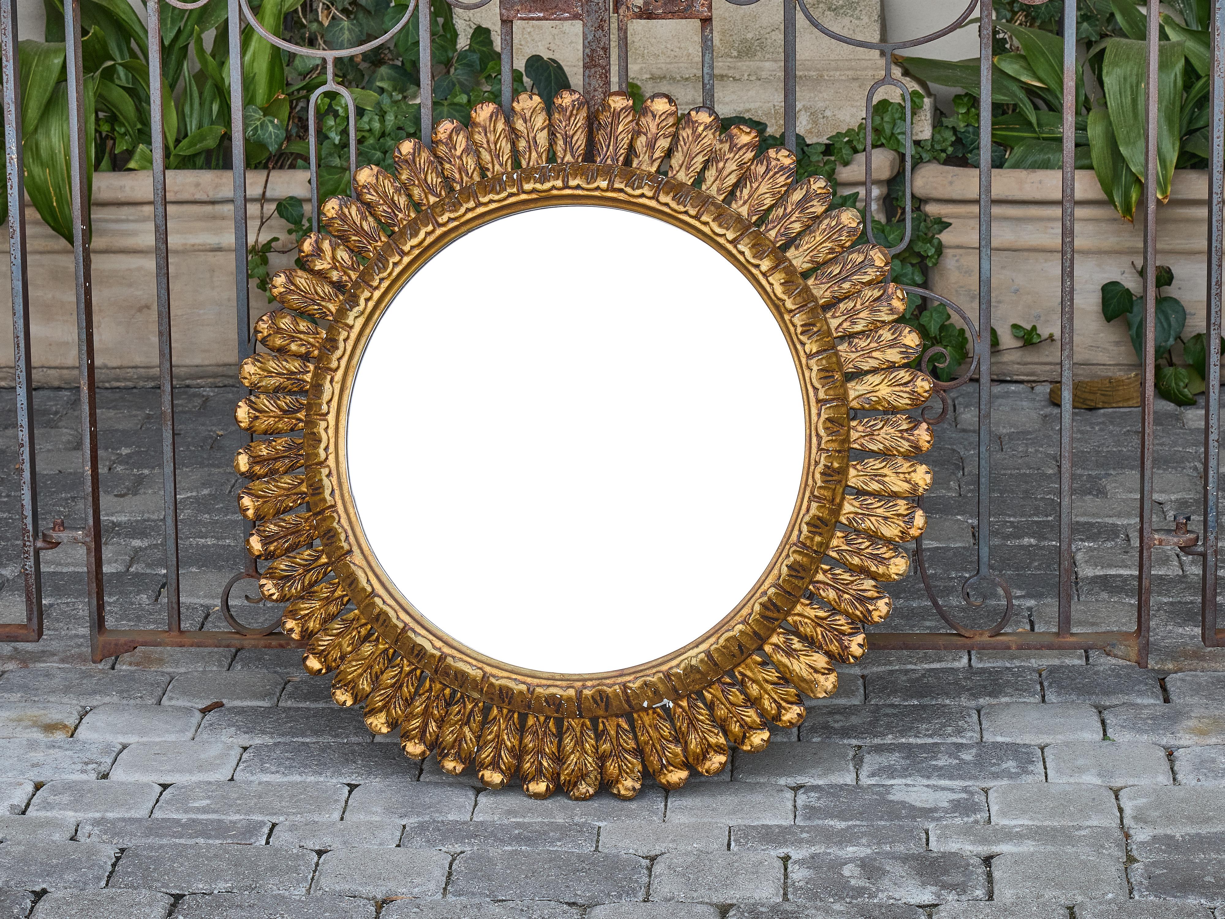 L'artigianato francese in legno dorato incontra l'estro scultoreo in questo sorprendente specchio rotondo risalente agli anni Venti. La cornice radiale è intagliata con un motivo a piume che ricorda i raggi del sole o le fronde di palma stilizzate,
