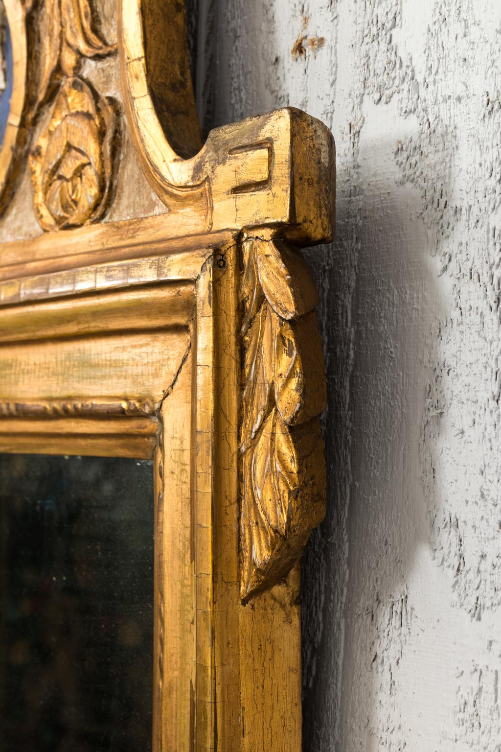 Giltwood Gustavian mirror that features an elaborately carved crown and base, circa late 19th century. The crown features a centre icon medallion of a female profile with floral carvings and ribbons.
   