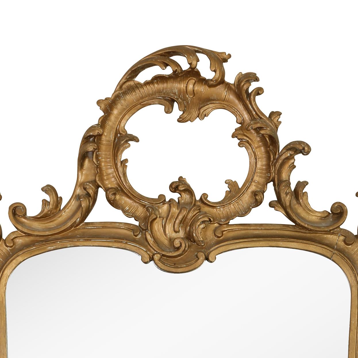 A vintage giltwood Italian mirror with natural patina. The large, rectangular mirror frame is decorated with giltwood scrolls and flourishes with foliate detail and an open round crest at the top.