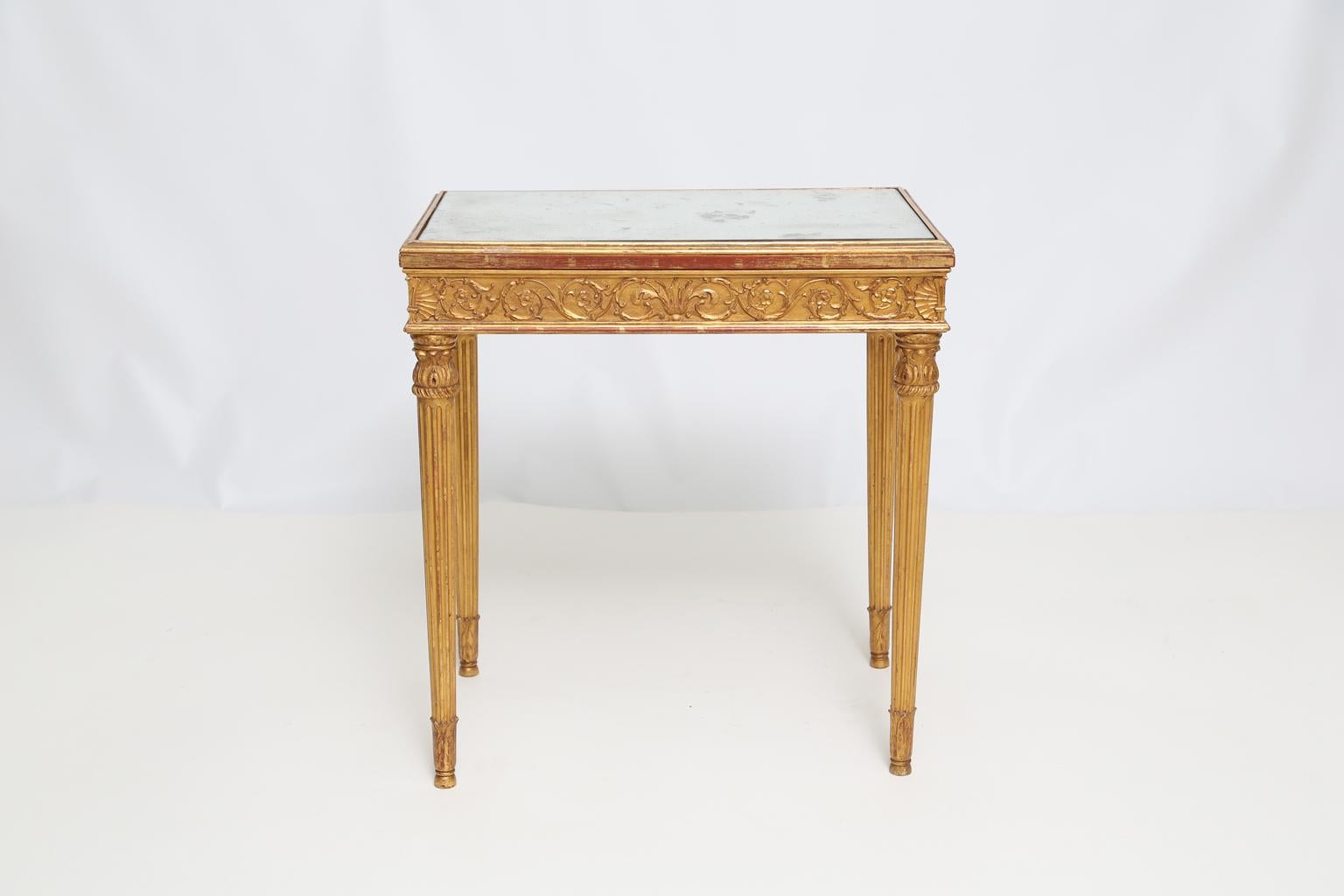 Accent table, having a rectangular top of aged mirror, on giltwood base, its apron carved with foliate scrollwork, raised on acanthne-headed, round, tapering, fluted legs, ending in touipe feet. 

Stock ID: D1562.