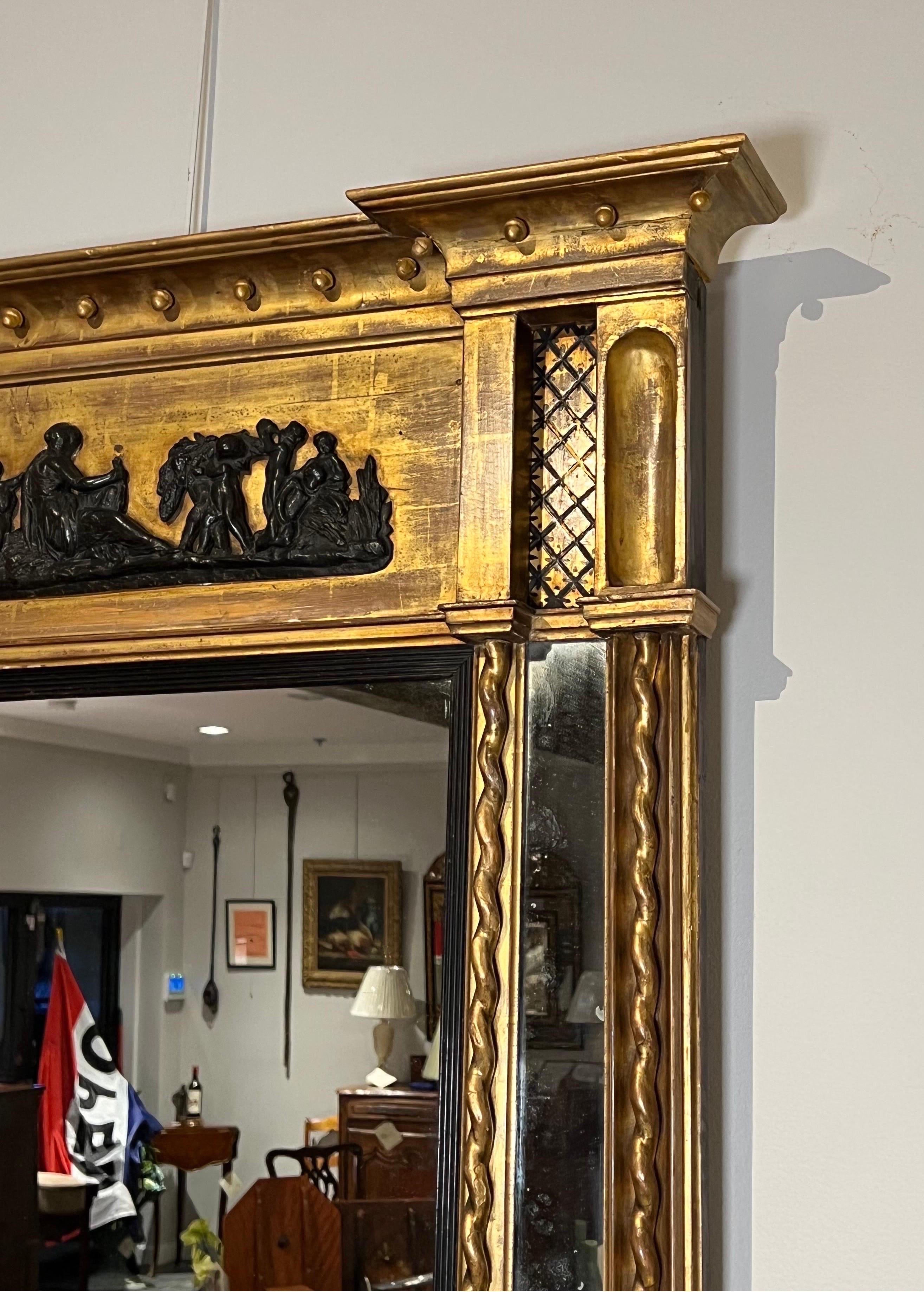 Miroir néoclassique en bois doré. Un grand miroir rectangulaire entouré de moulures ébénisées, flanqué de 2 panneaux plus petits sous un panneau de composition ébénisé sous une moulure en couronne à glands et dorures.