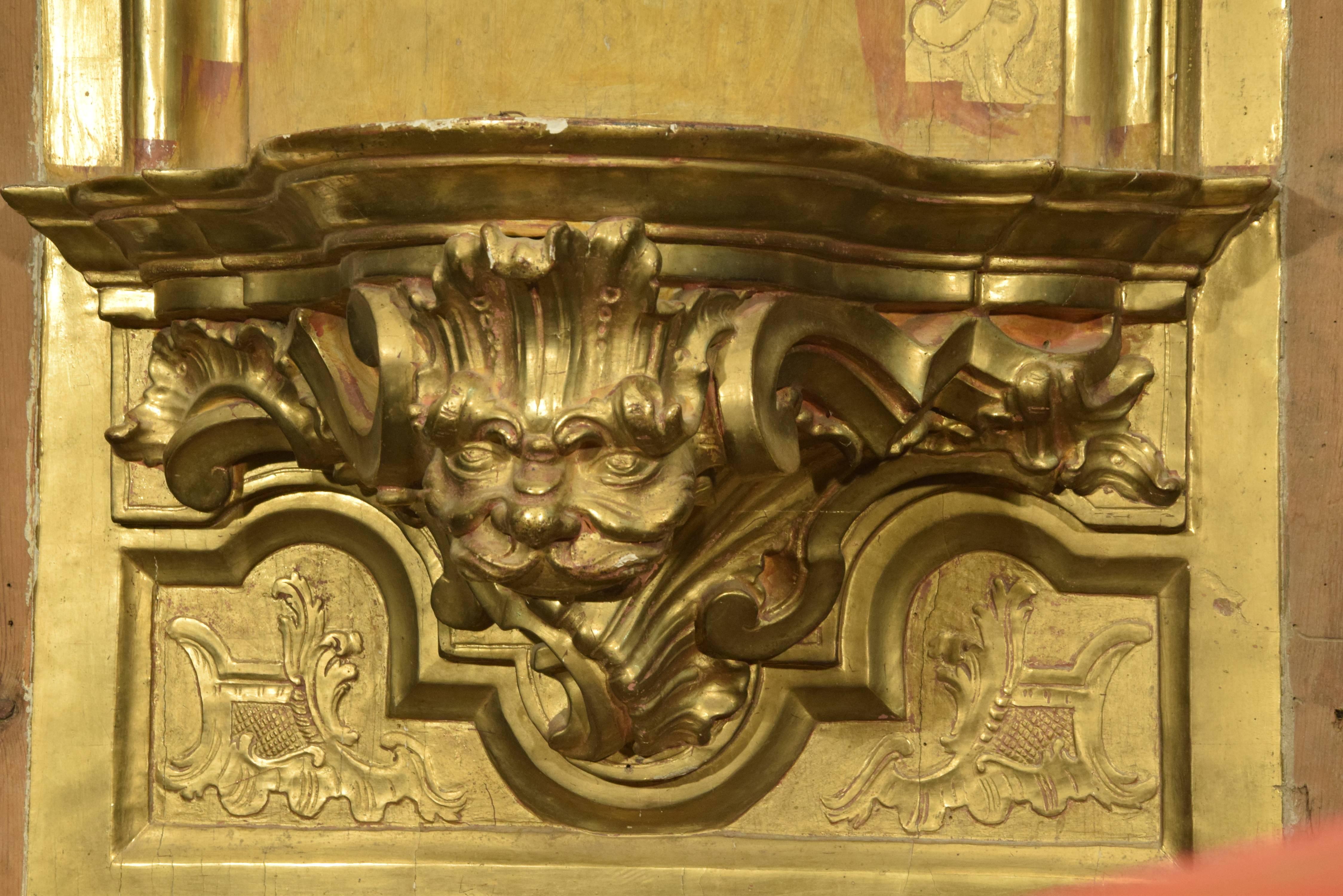 Hornacina formée d'un fond décoré de moulures et d'un support pour une sculpture décorée d'un masque et de motifs végétaux et surmontée d'un fronton fendu avec un motif central travaillé sur son fond ressemblant à une étoffe. Des cornes d'abondance