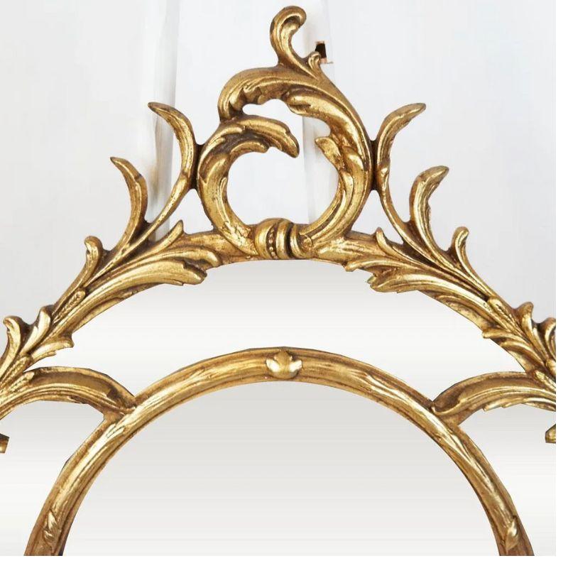 An oval giltwood mirror with scroll motif.  A double frame mirror with a beveled edge to the larger, center mirror and a rocaille scroll motif to the frame.  Fashioned after a fine 18th Century English artisan, John Linnell.