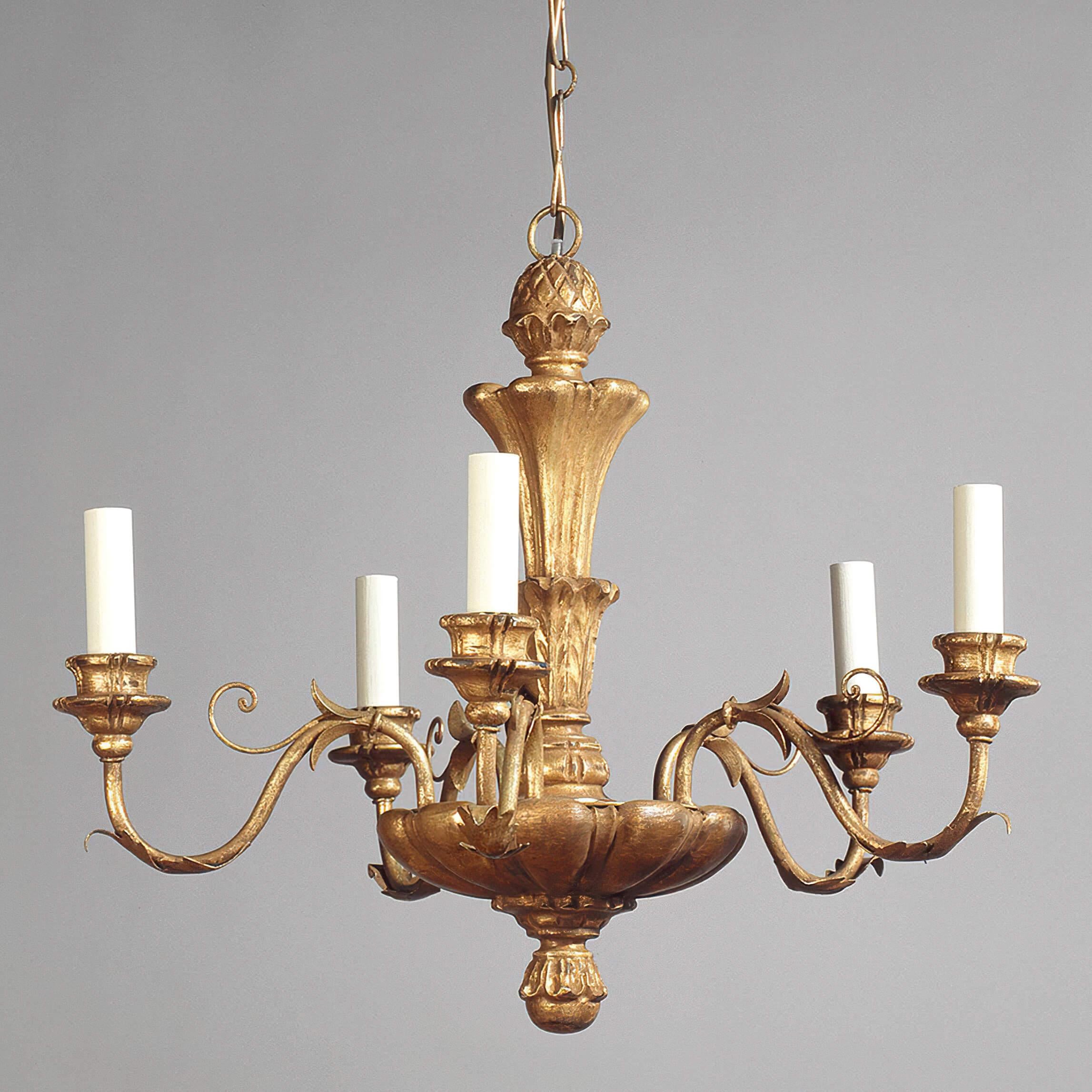 Based on a 17th-century antique, this chandelier is petite in scale and hand-finished in gilt. The hand-carved detailing, from the pineapple finial at the top to the flower at the base, adds character. The arms are fabricated from steel and wood for