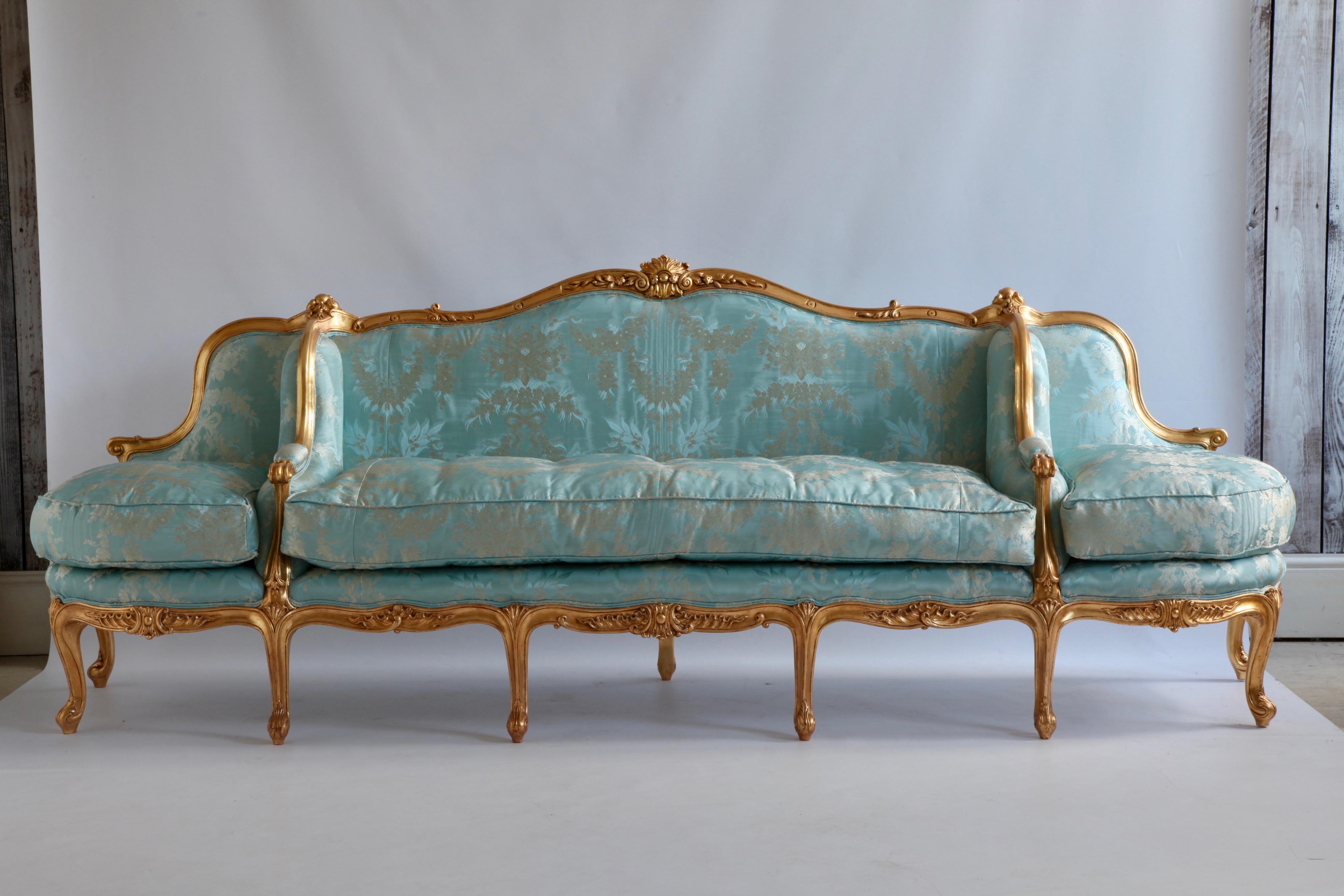 An elegant and impressive large Louis XV style confidante sofa which has been hand carved and gilded using traditional methods and materials to achieve an authentic period finish. The comfort of the sofa is enhanced with feather and down for the