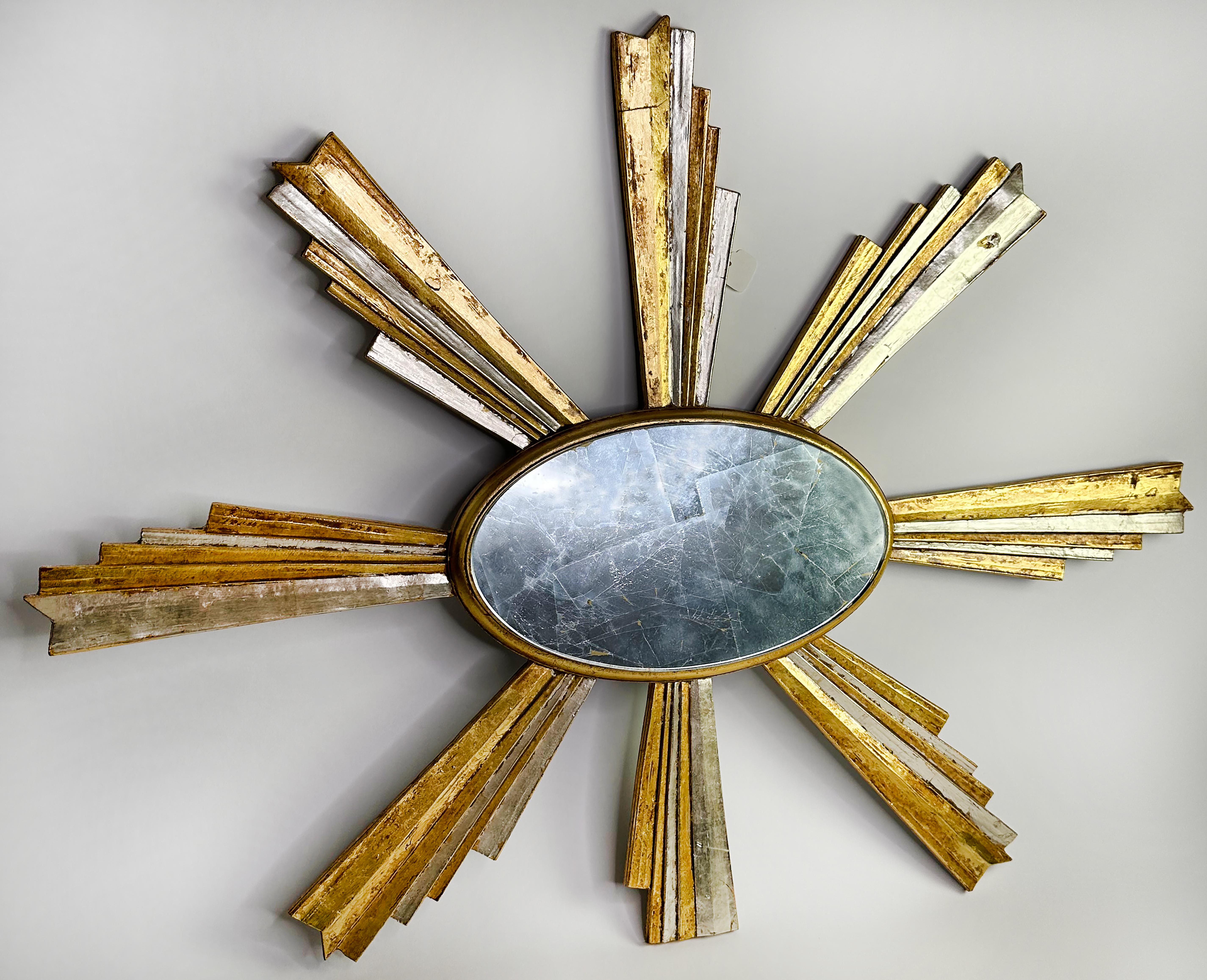 An elegant giltwood sunburst shaped oval framed wall mirror. Made some time between the late 1990s and the early 2000s. Created in an Art Deco style.

In good condition. Some gentle wear consistent with age and use. This bold and unique