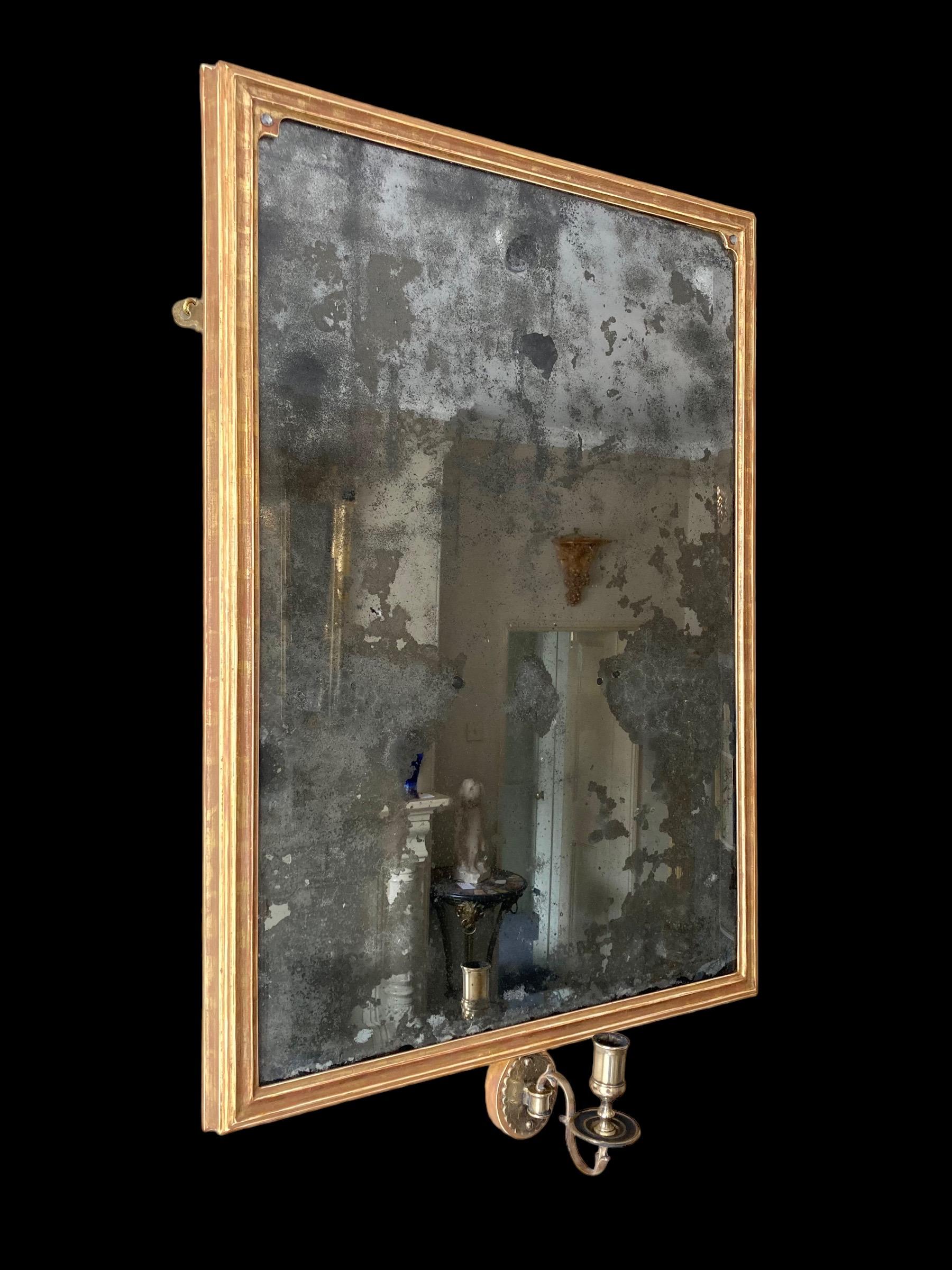 Ein auffälliger rechteckiger Wandspiegel aus vergoldetem Holz mit einem einzigen Kerzenarm.
Die stark stockfleckige Quecksilberspiegelplatte mit abgeschrägtem Rand aus dem 18. Jahrhundert befindet sich in einem späteren klassischen rechteckigen
