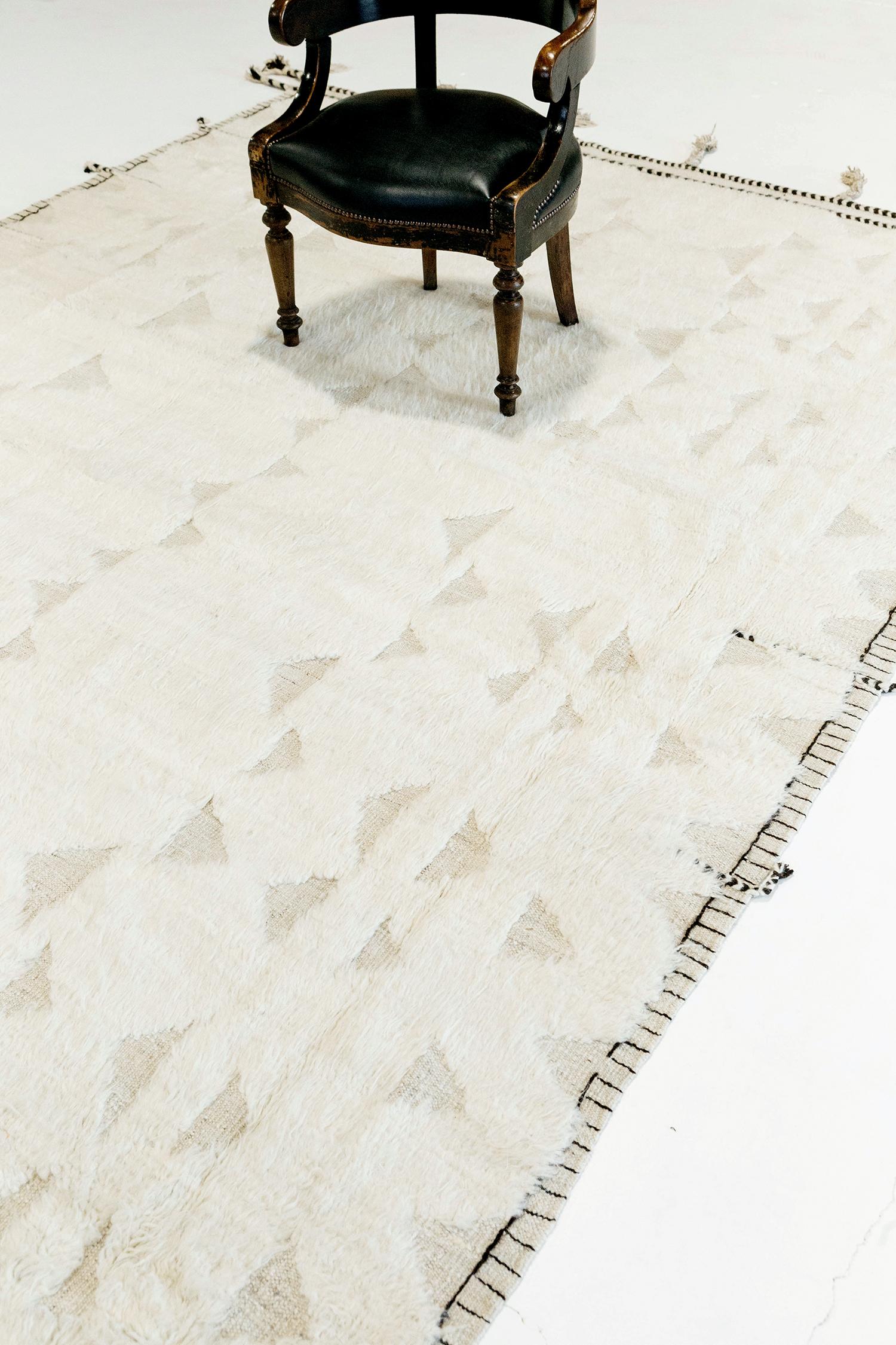 Gimbrala' est un superbe tapis naturel ivoire tissé à la main, avec des détails en forme de triangle en relief entourant un velours blanc parfait. De magnifiques glands et des motifs bordés ajoutent une essence opportune et unique au monde du design