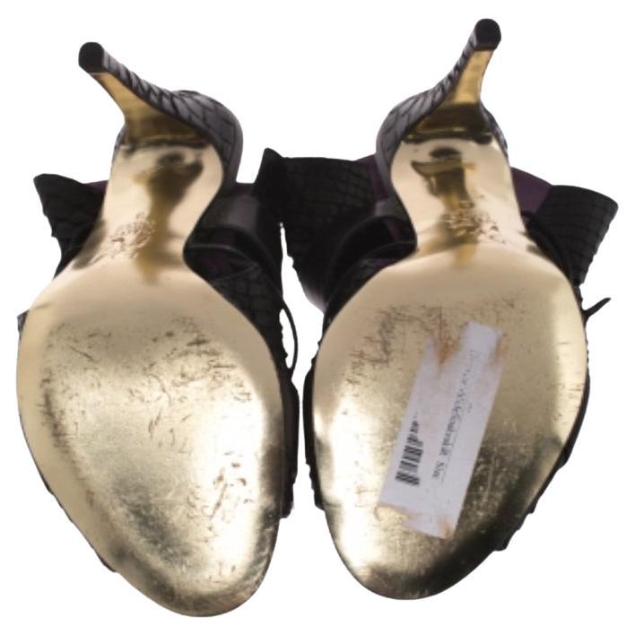 Crea i look più accattivanti per le feste indossando queste elegantissime mules Gina. Realizzati in pelle di pitone nera, questi sandali dal tacco vertiginoso presentano cinturini in pelle con fibbie sulla tomaia e sulla punta. Sfoggia un look