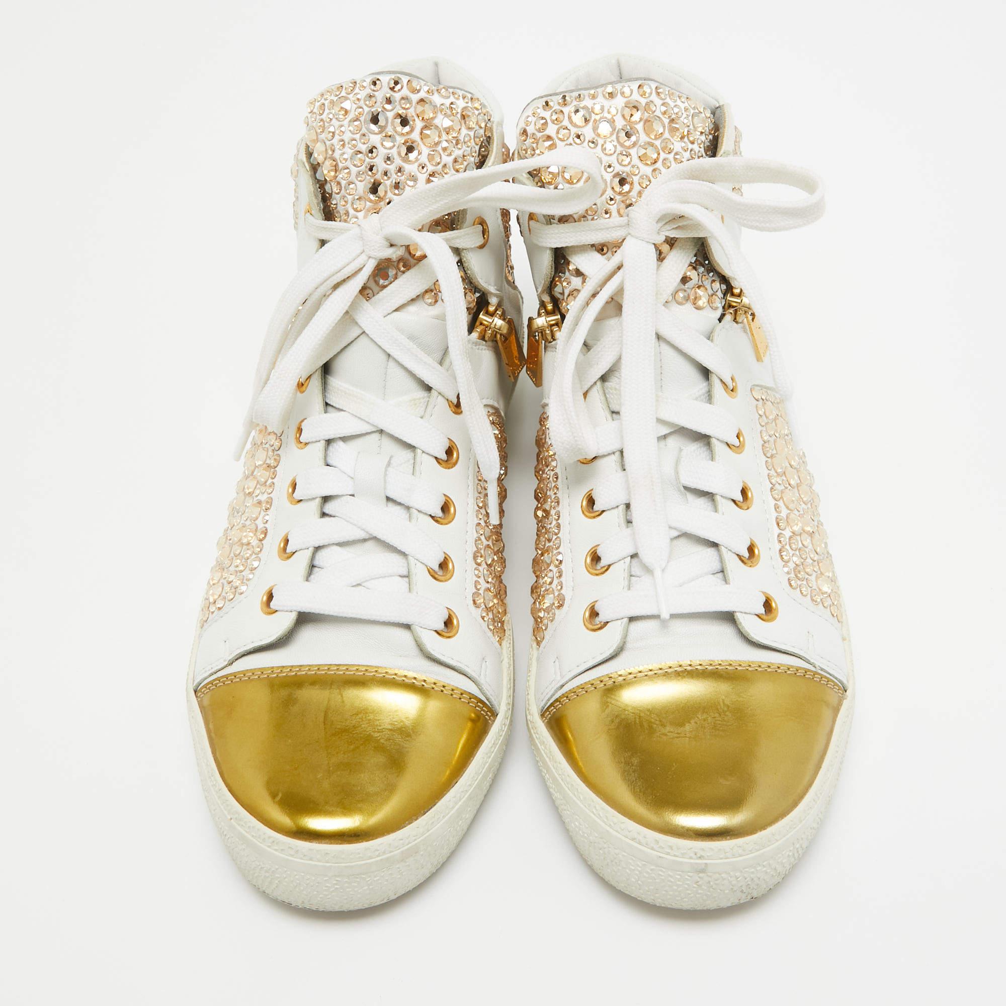 Un peu de flash peut être vraiment modulable et c'est le cas de ces baskets montantes de Gina. Elle a été réalisée en cuir blanc avec des finitions dorées et est ornée de strass dorés sur l'ensemble de sa surface. Les semelles sont doublées de