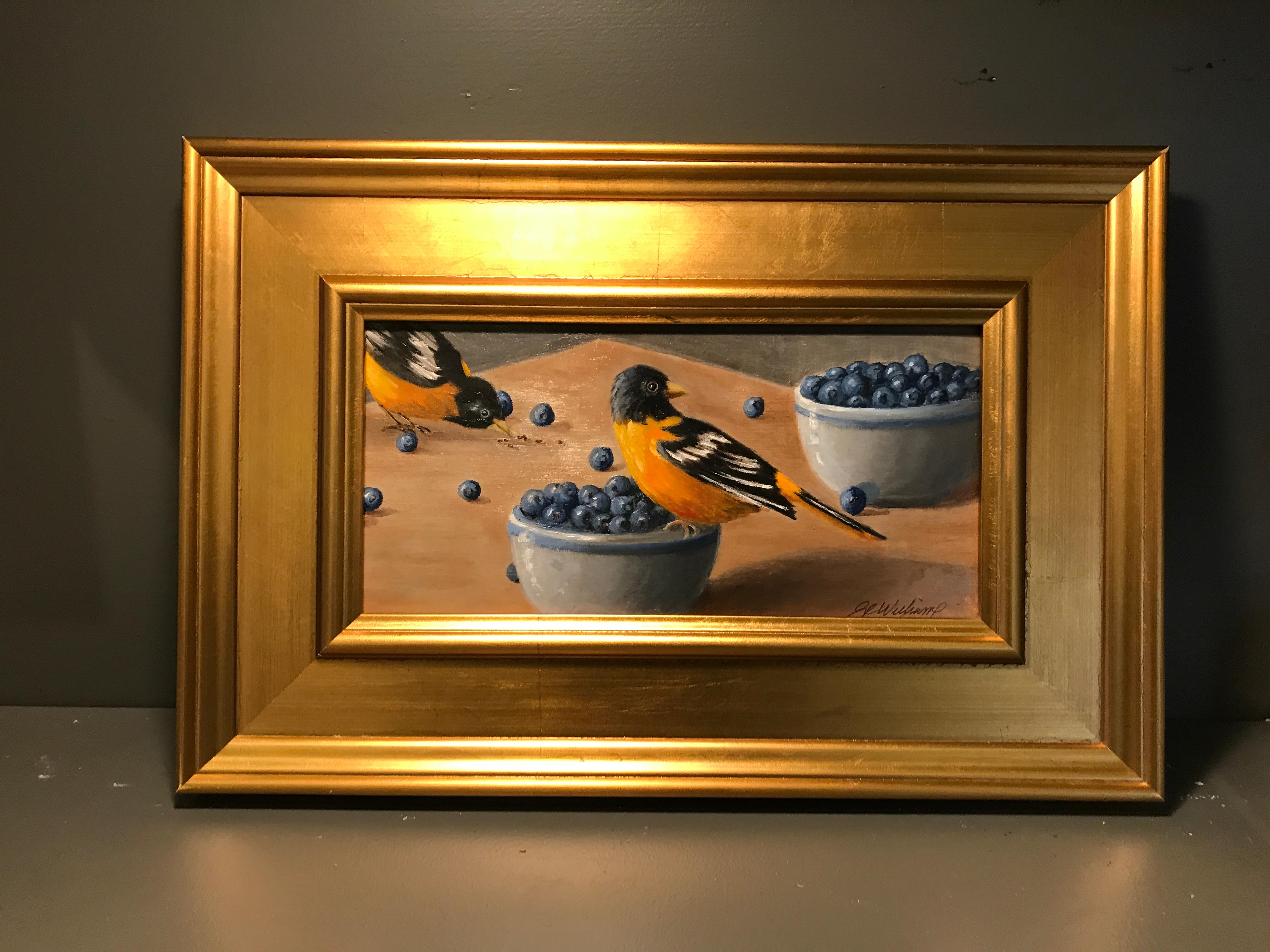 'Birds of a Feather' is a small gilt framed oil on board painting created by American artist Ginny Williams in 2018. Featuring a palette made of orange, blue, black and grey tones, this painting depicts two lovely birds pecking at blueberries.