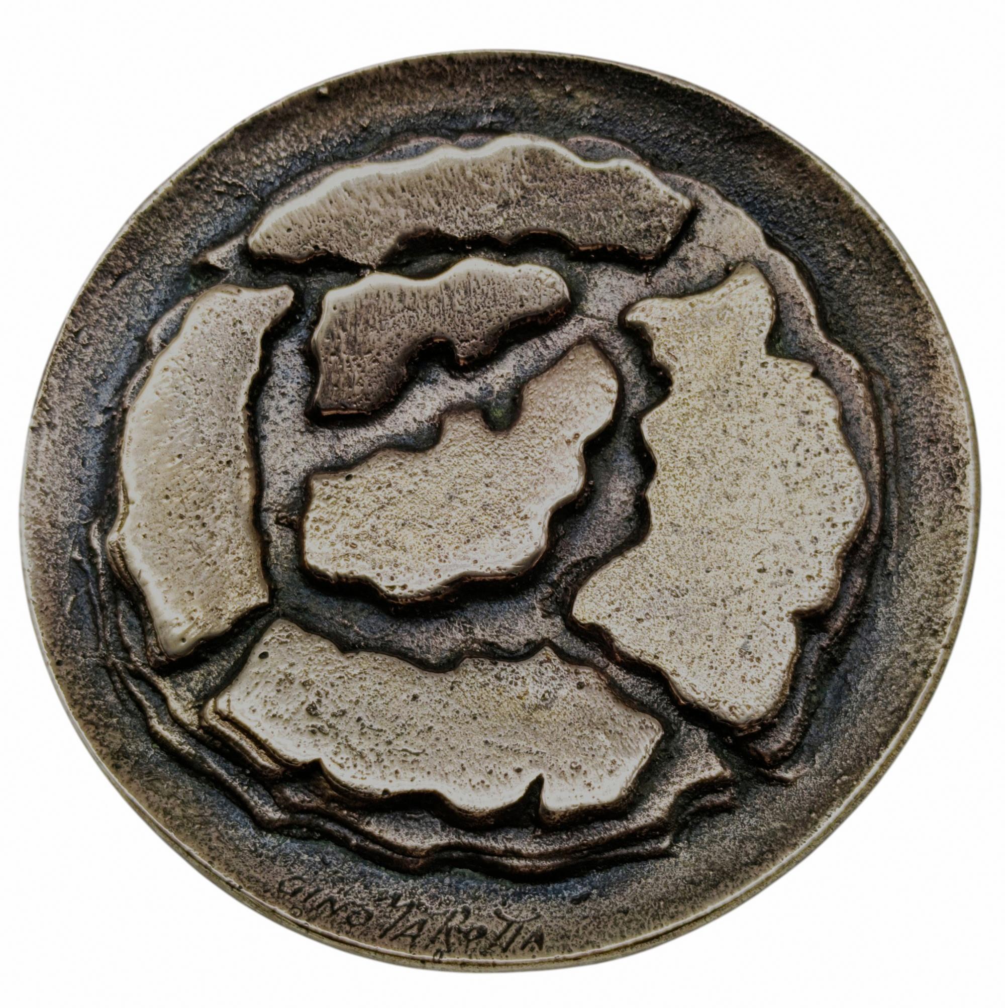 Vom Künstler Gino Marotta entworfenes Bronzemedaillon, das eine stilisierte Rose darstellt. Gino Marotta (Campobasso, 1935 - Rom, 2012) war ein italienischer Maler und Bildhauer. Nach einer anfänglichen Periode, in der er sich der informellen Kunst