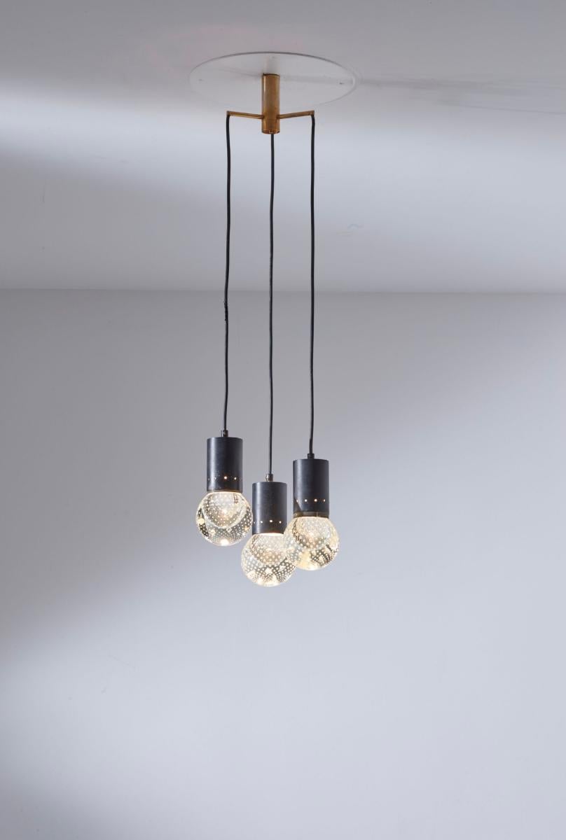 This chandelier is model 2042/3, designed by Gino Sarfatti for Arteluce in 1963.
It is a three-light pendant with a minimalist and refined structure.
Three black cables of varying lengths extend from the circular satin-finish brass ceiling
