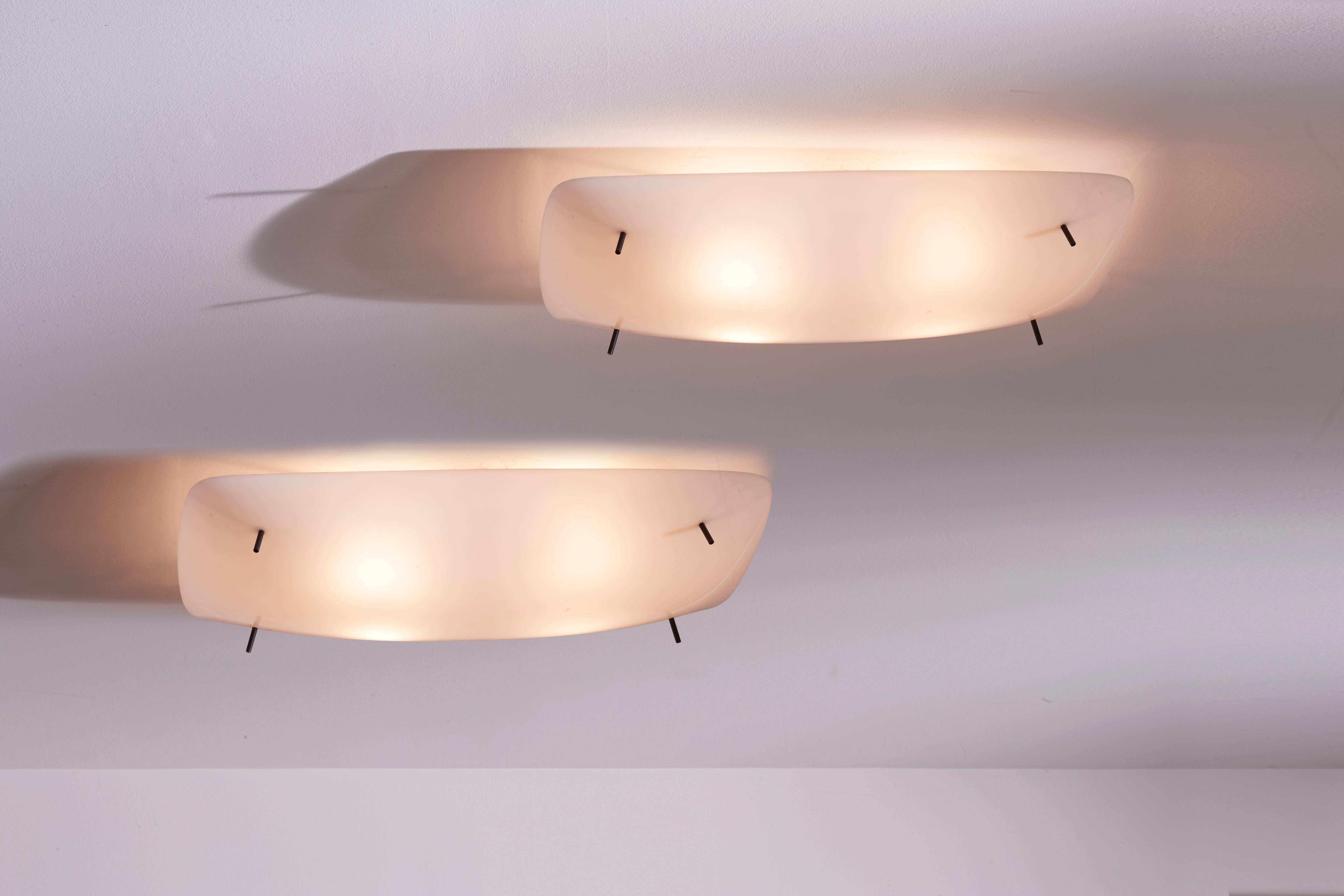 A rare pair of sconces, model 3032/F, designed by Gino Sarfatti for Arteluce in 1954. Crafted from a blend of metal and white methacrylate, these ceiling lamps embody mid-century modern aesthetics.

Featuring a slightly concave rectangular shape,