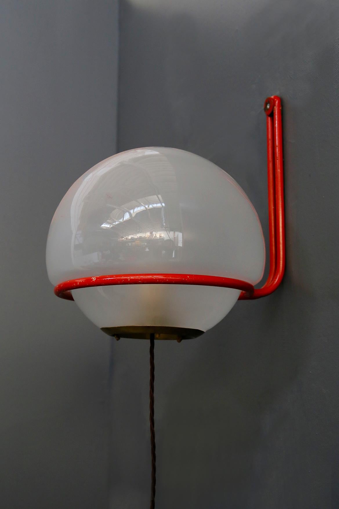 Important and published wall lamp of 1950s. The lamp is designed by Gino Sarfatti for Arteluce. The ceiling lamp is in satin glass with a rounded shape. To support it on the wall there is a red painted aluminium tube that surrounds the sphere. The