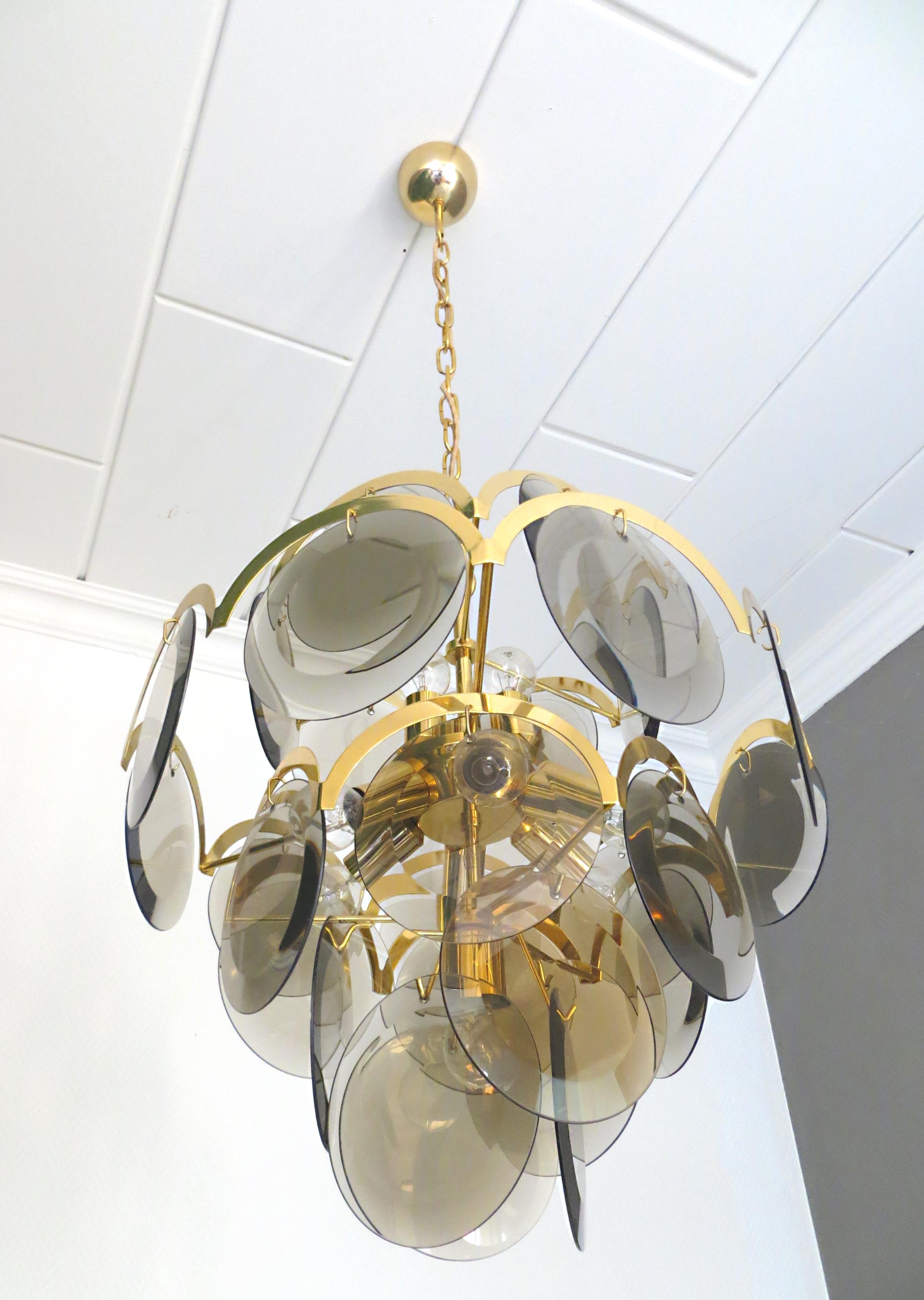 We are offer you an vintage chandelier by Gino Vistosi from Italy, 1970s - 1980s . These hanging lamp have four tiers, with round smoke
disc glass, framed by half moon gilded or gilt shaped brass.
It has 27 glass discs and 10 light bulbs, for an