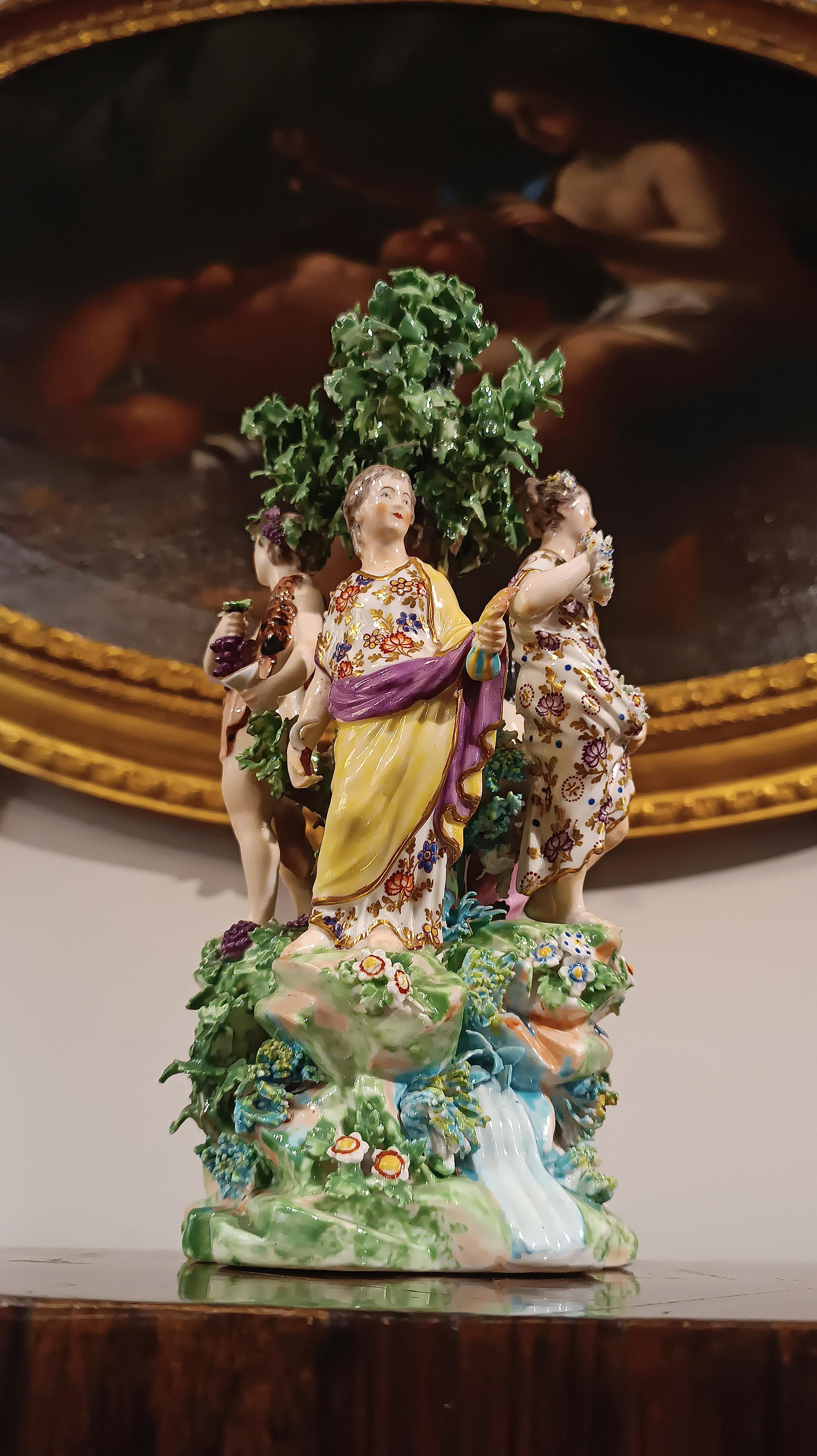 Wonderful polychrome porcelain sculpture depicting the allegory of the four seasons. The figures personifying winter, autumn, spring and summer are harmoniously arranged around a tree on an idyllic hill, surrounded by flowers and streams. Winter is